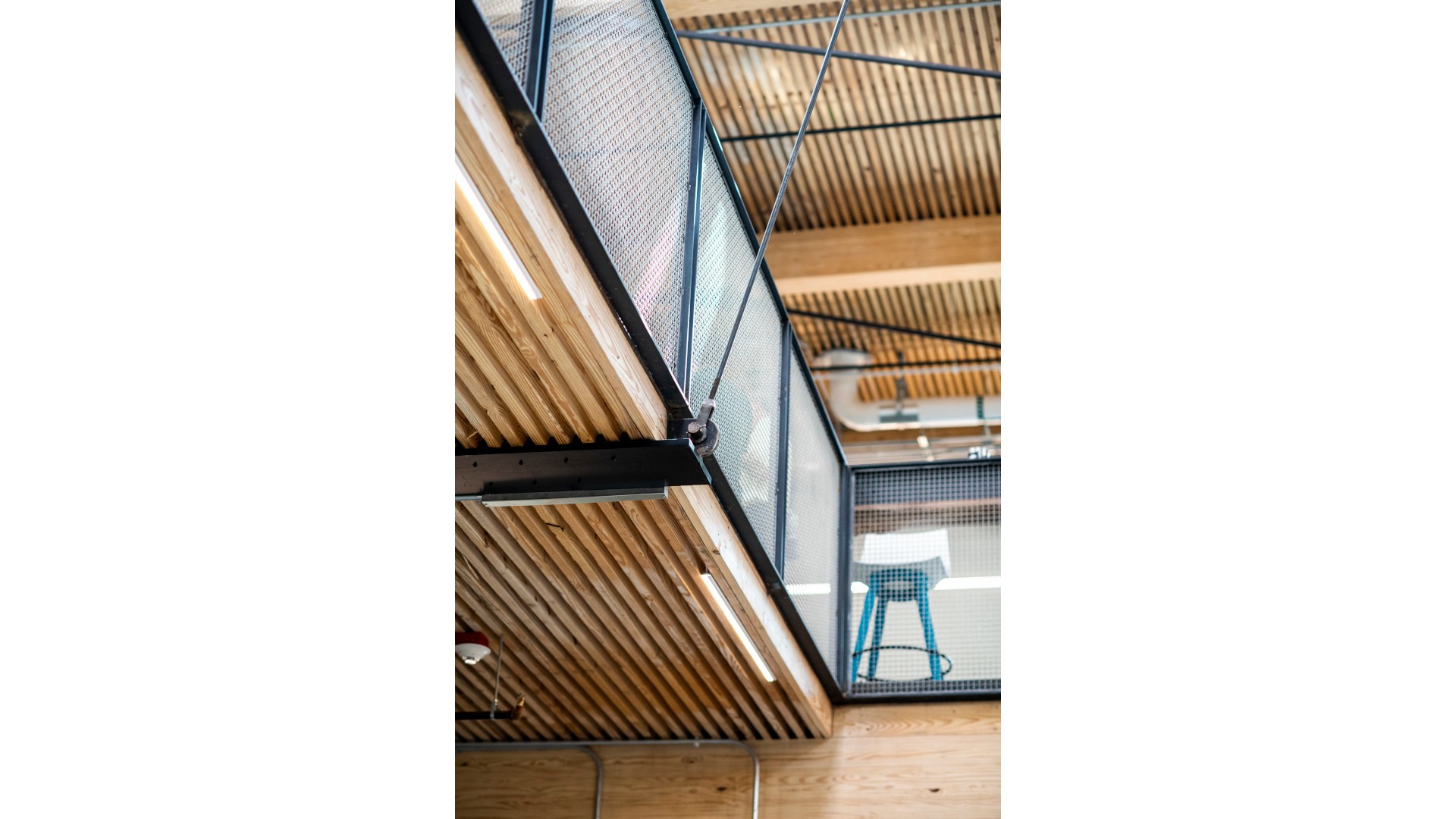 Modern loft interior with wooden slatted ceiling, black metal railings, and blue bar stool.