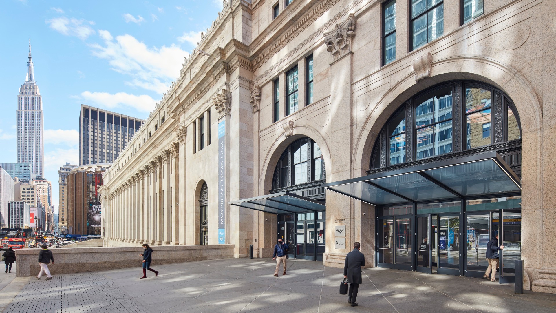 Exterior view of Moynihan Train Hall with the Empire State Building in the background.