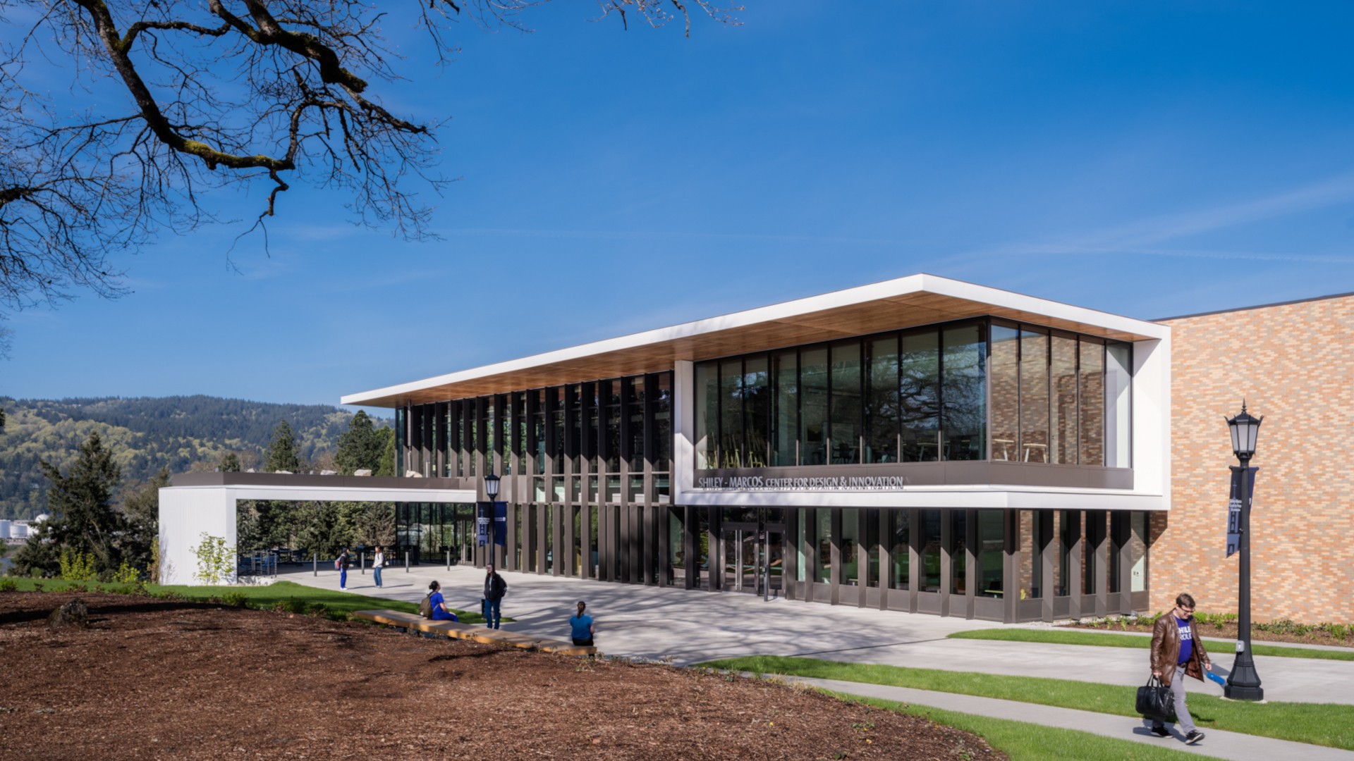 Modern educational building with large windows and a walkway, set against a clear blue sky.