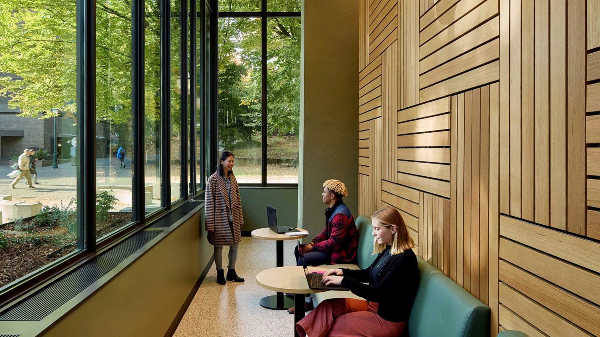 The Portland State University – Vernier Science Center Modern office lounge with large windows, featuring three individuals engaged in conversation.