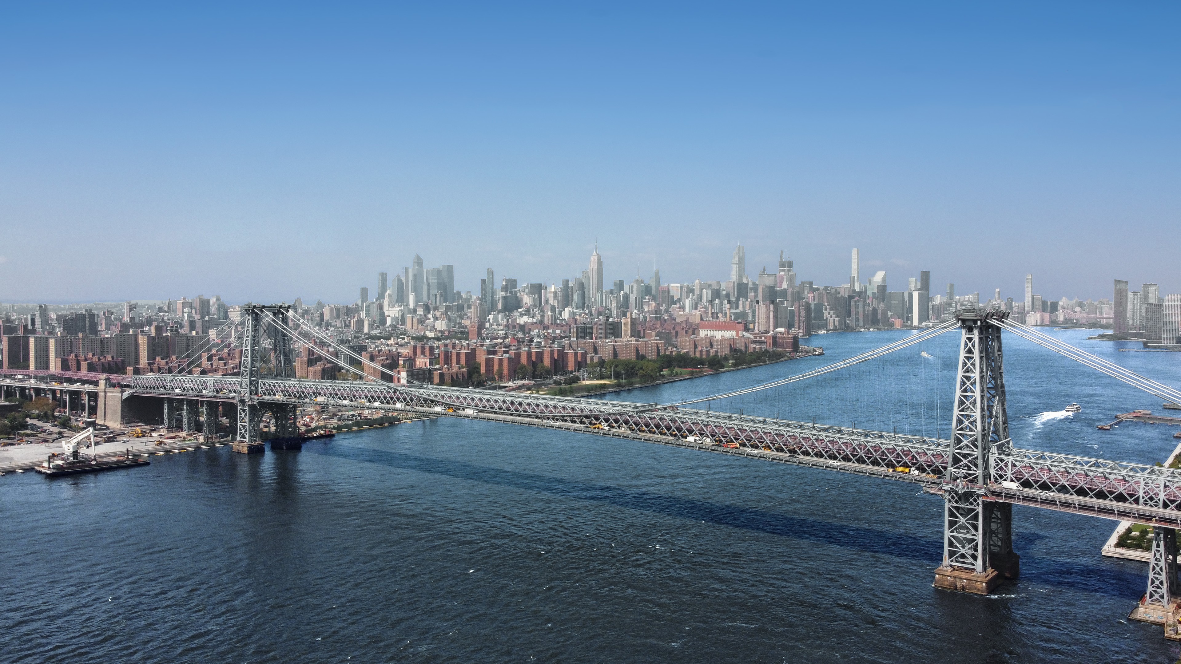 Aerial view of the Williamsburg Bridge spanning the East River with Manhattan skyline in background.