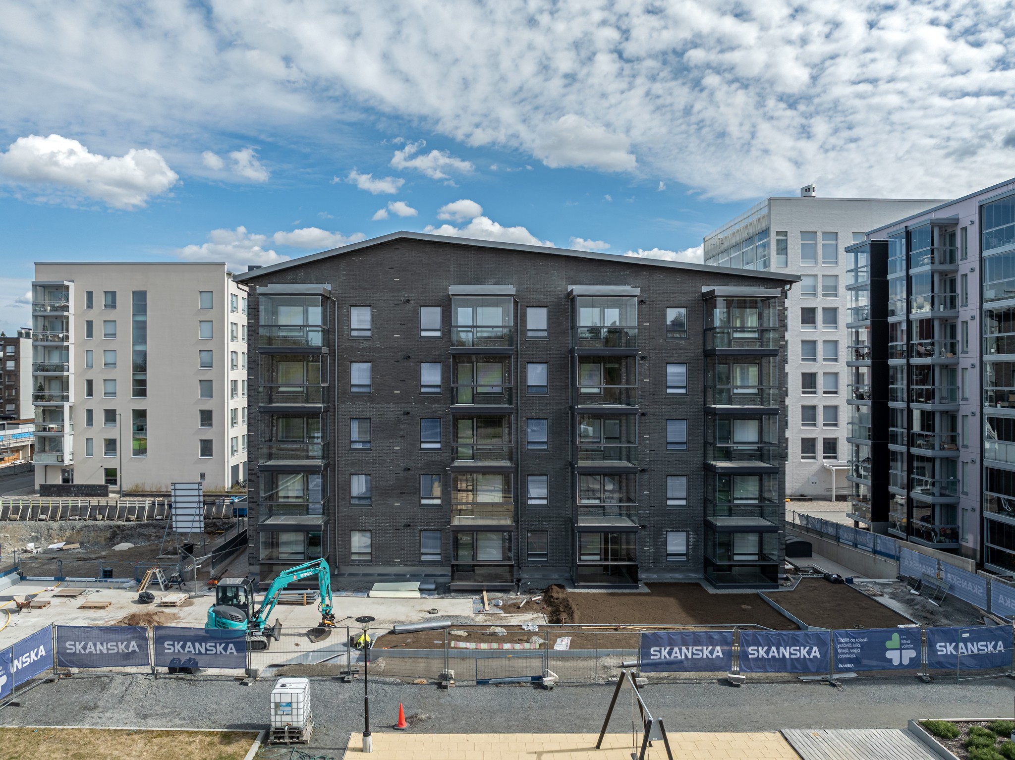 Modern apartment building under construction with Skanska barriers and machinery in front.