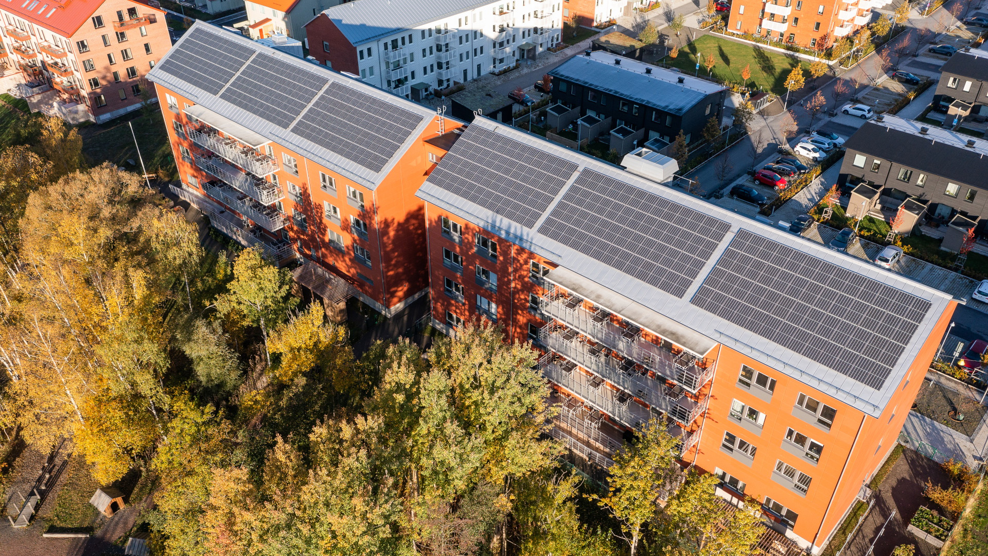 Aerial view of orange apartment buildings with solar panels on roofs surrounded by trees.