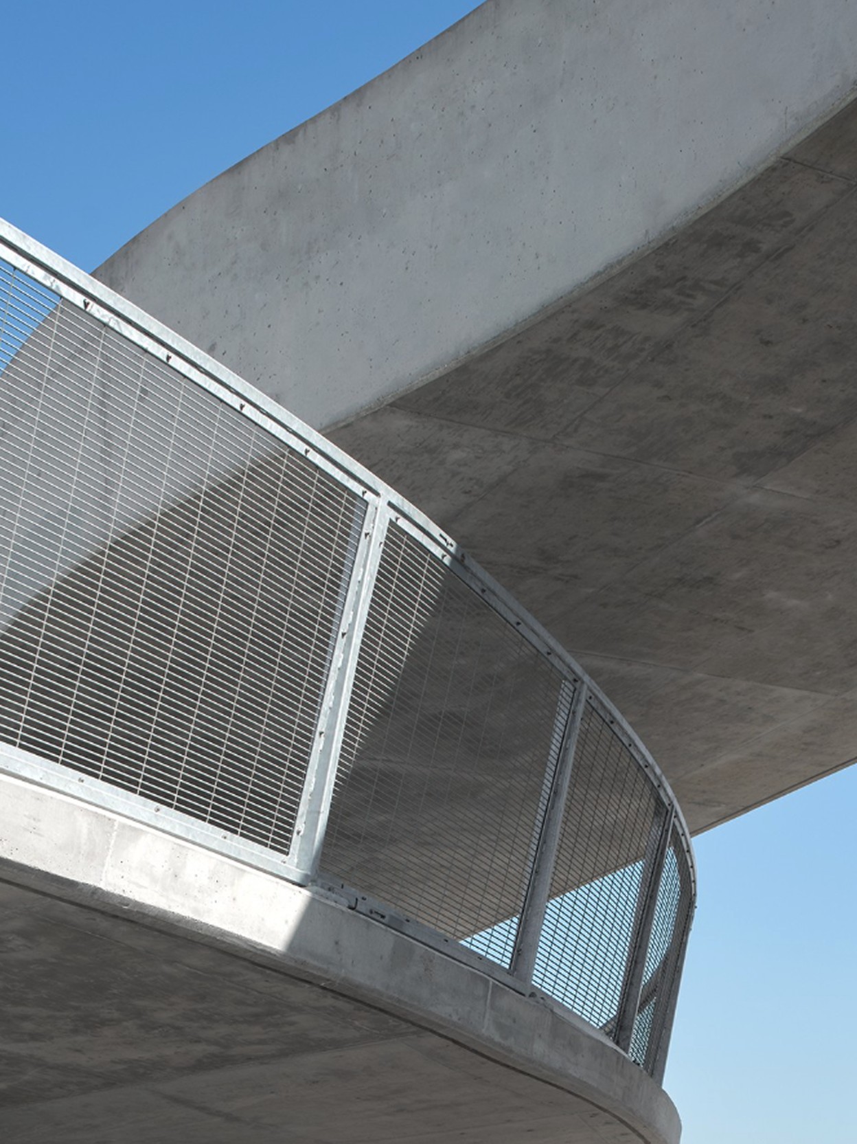 Modern concrete walkway with metal railing curves under blue sky.