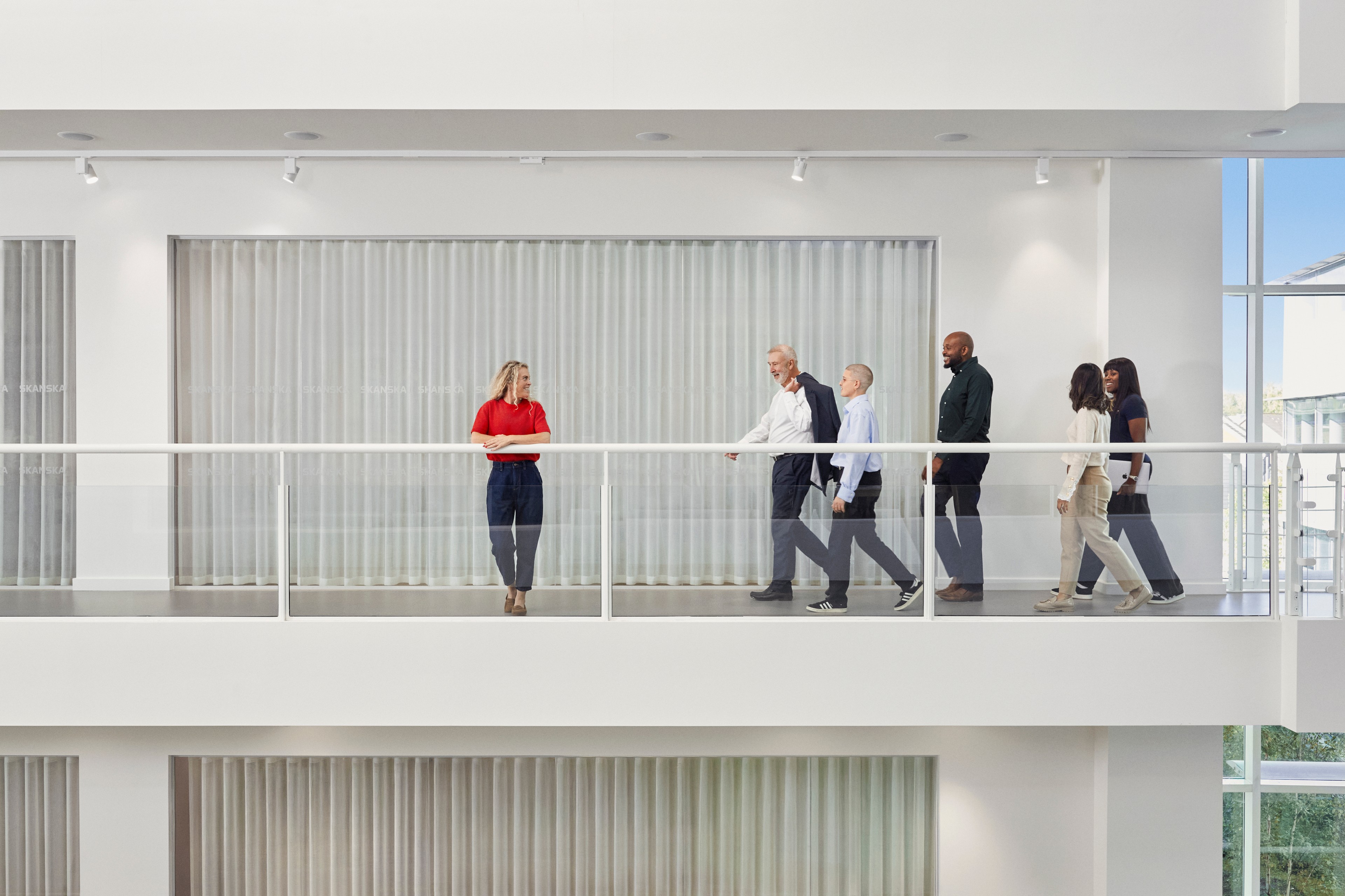 Diverse group of business professionals walking in modern office hallway with glass railing.