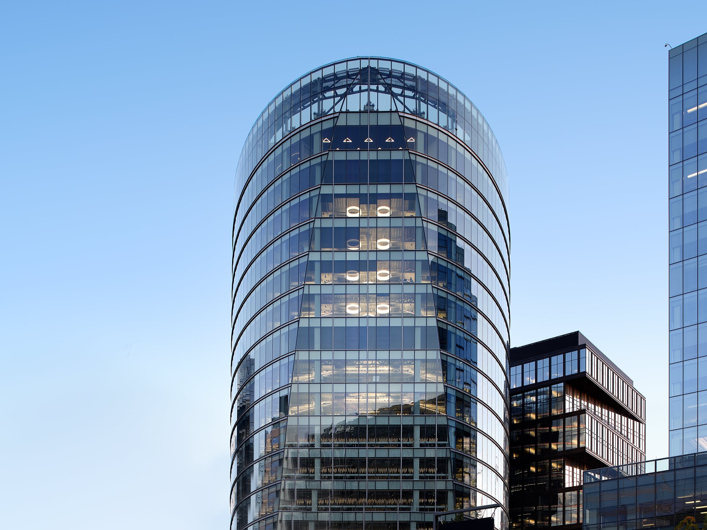 Modern glass office building with curved edges under a clear blue sky in a cityscape.