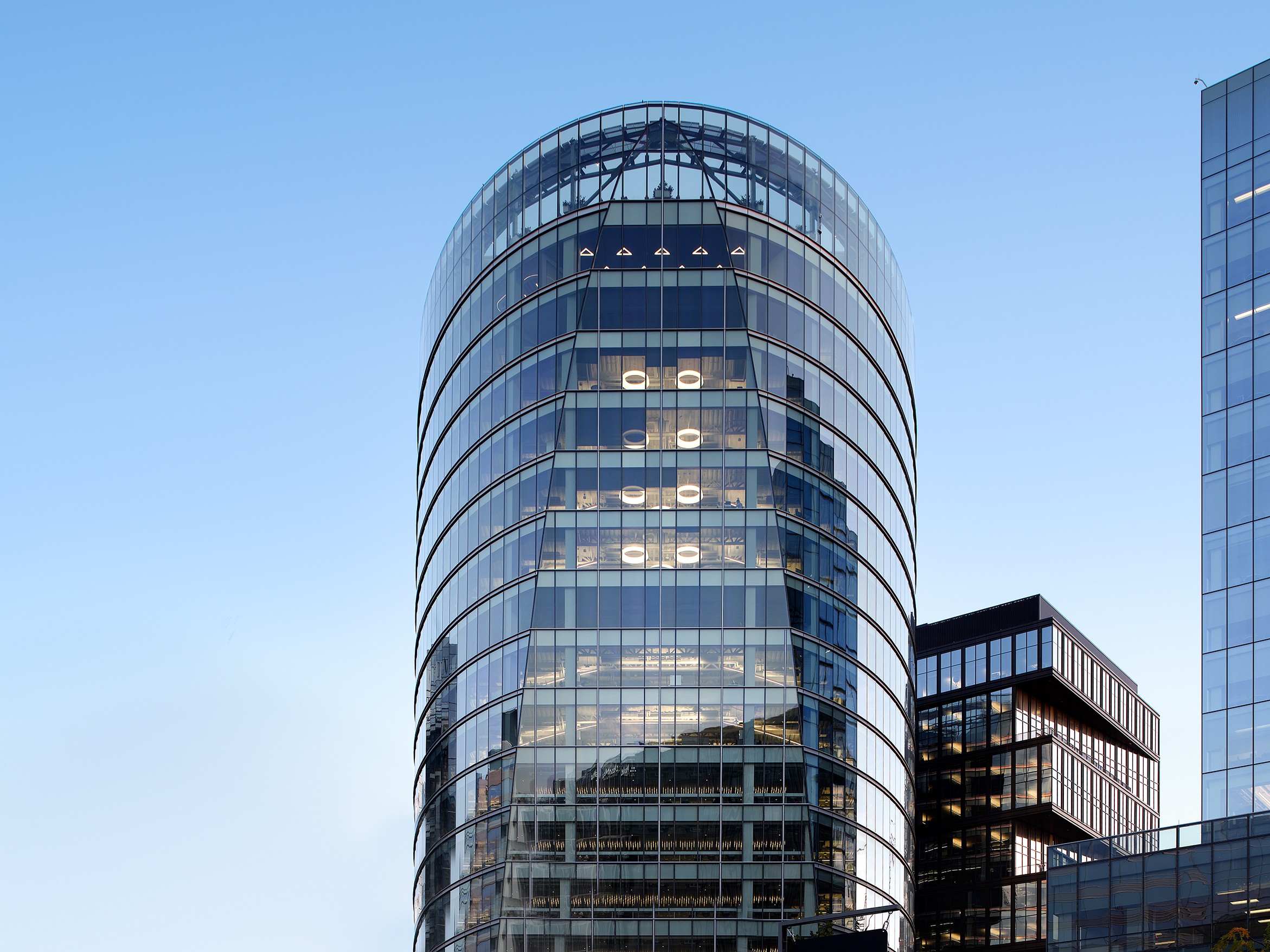 Modern glass office building with curved edges under a clear blue sky in a cityscape.