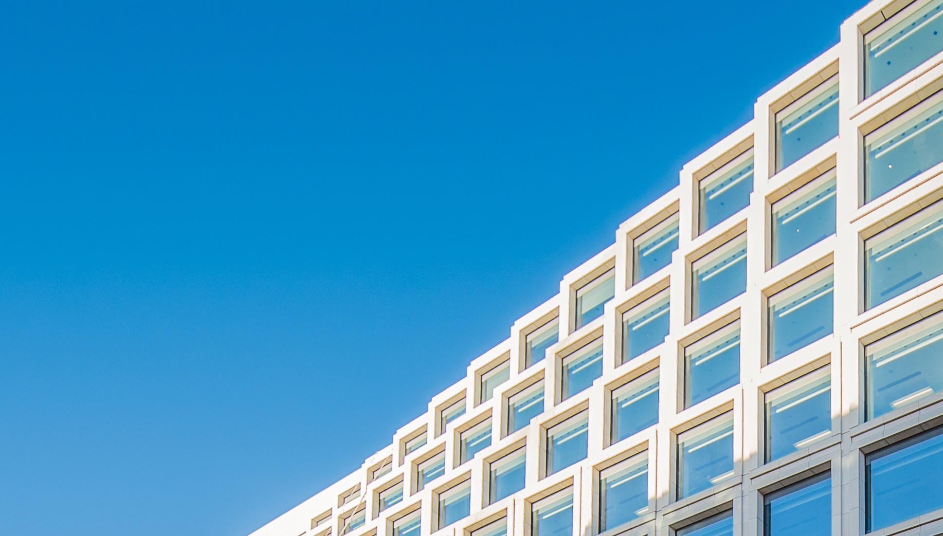 Modern kontorsbyggnad med stora glasfönster under en klar blå himmel.