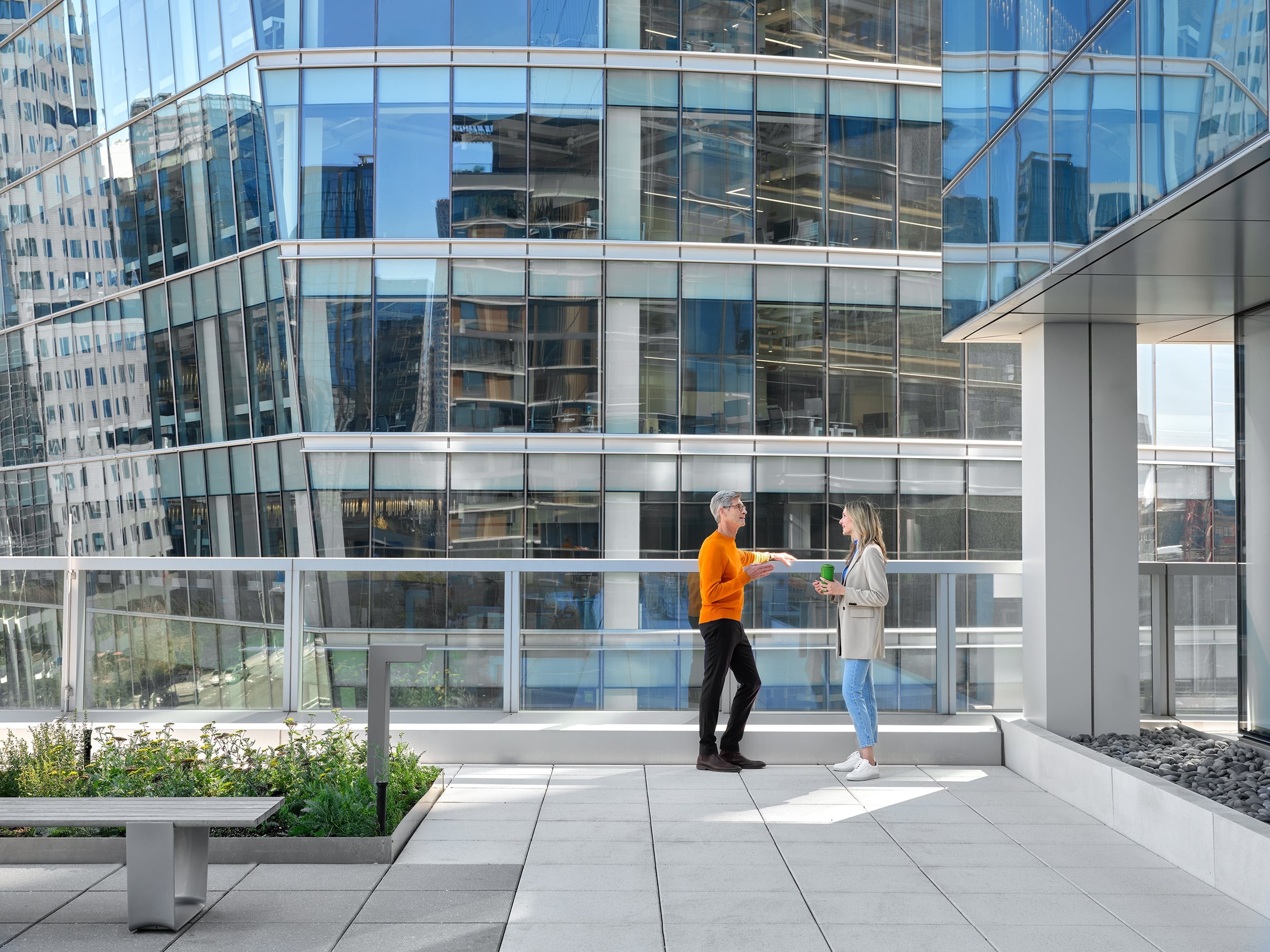 Two people exchanging documents on a modern office building rooftop terrace.