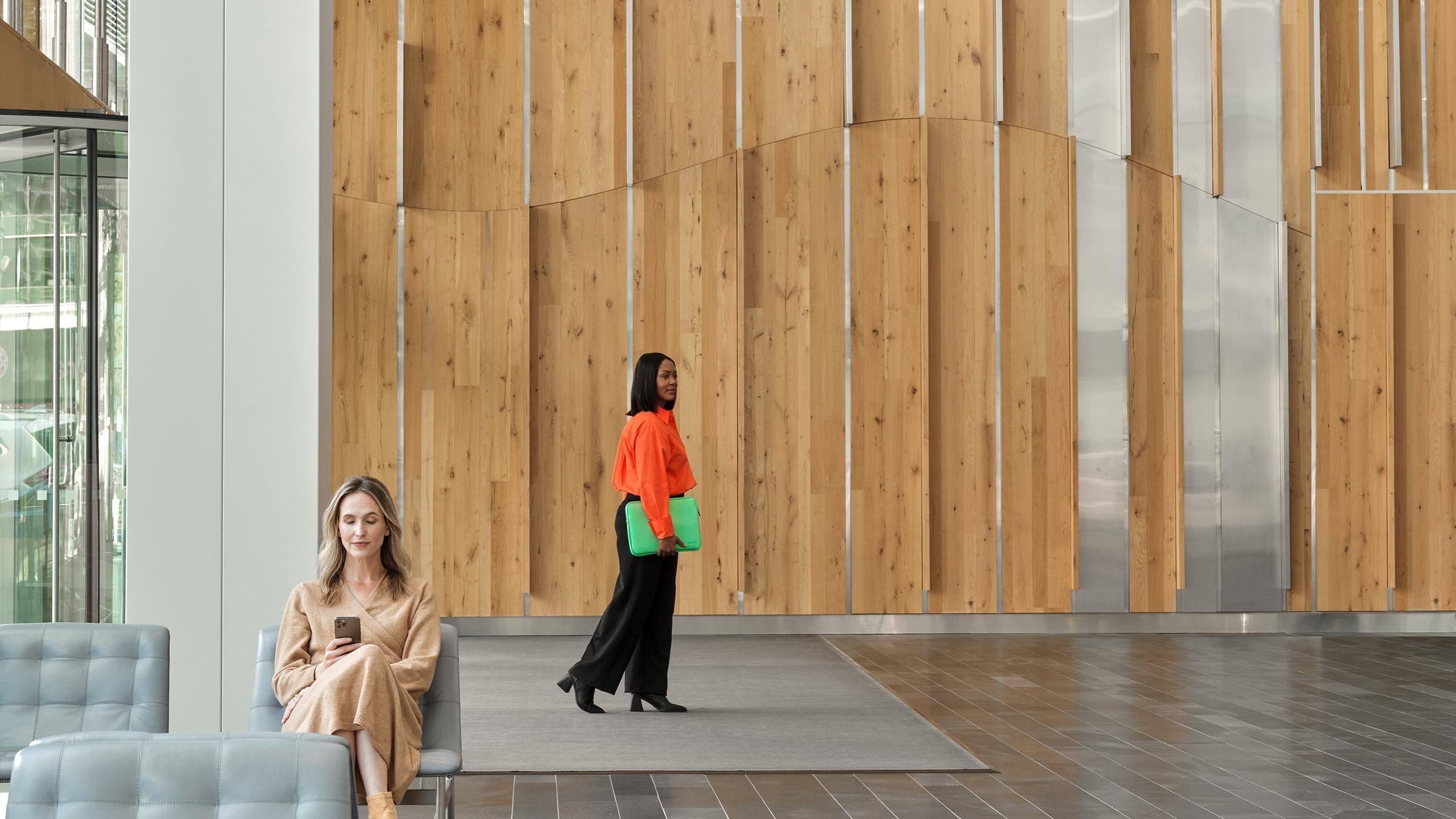 Two women in a modern wooden-paneled office lobby, one standing and one seated.