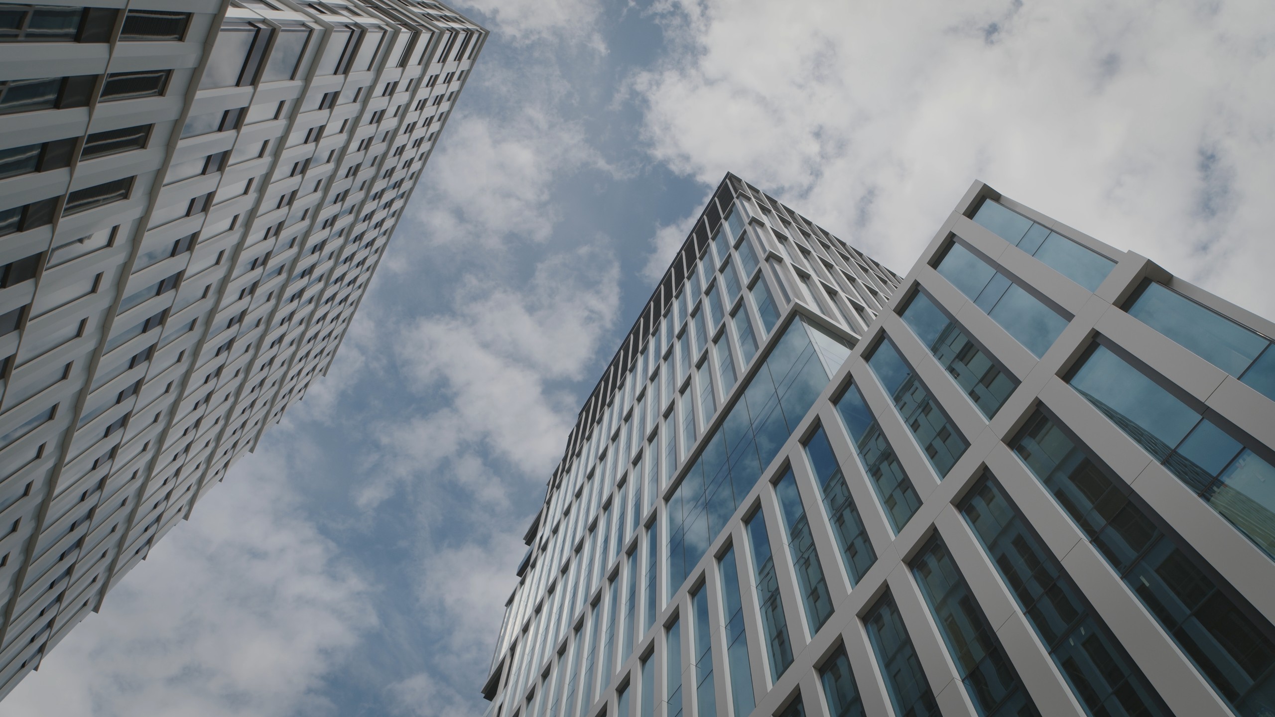 Modern skyscrapers with glass windows against a cloudy sky, showcasing urban architecture.