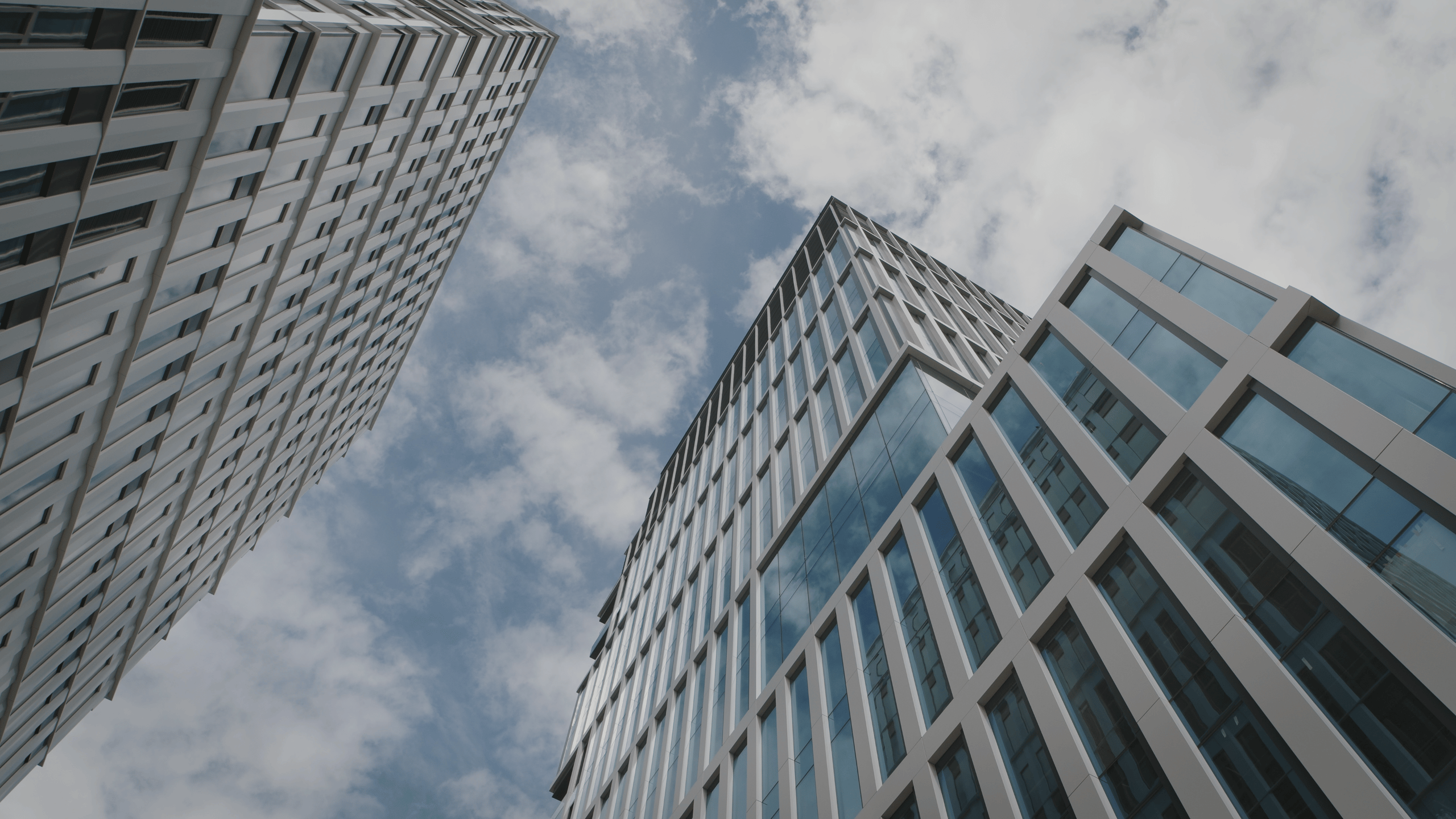 Modern skyscrapers with glass windows against a cloudy sky, showcasing urban architecture.
