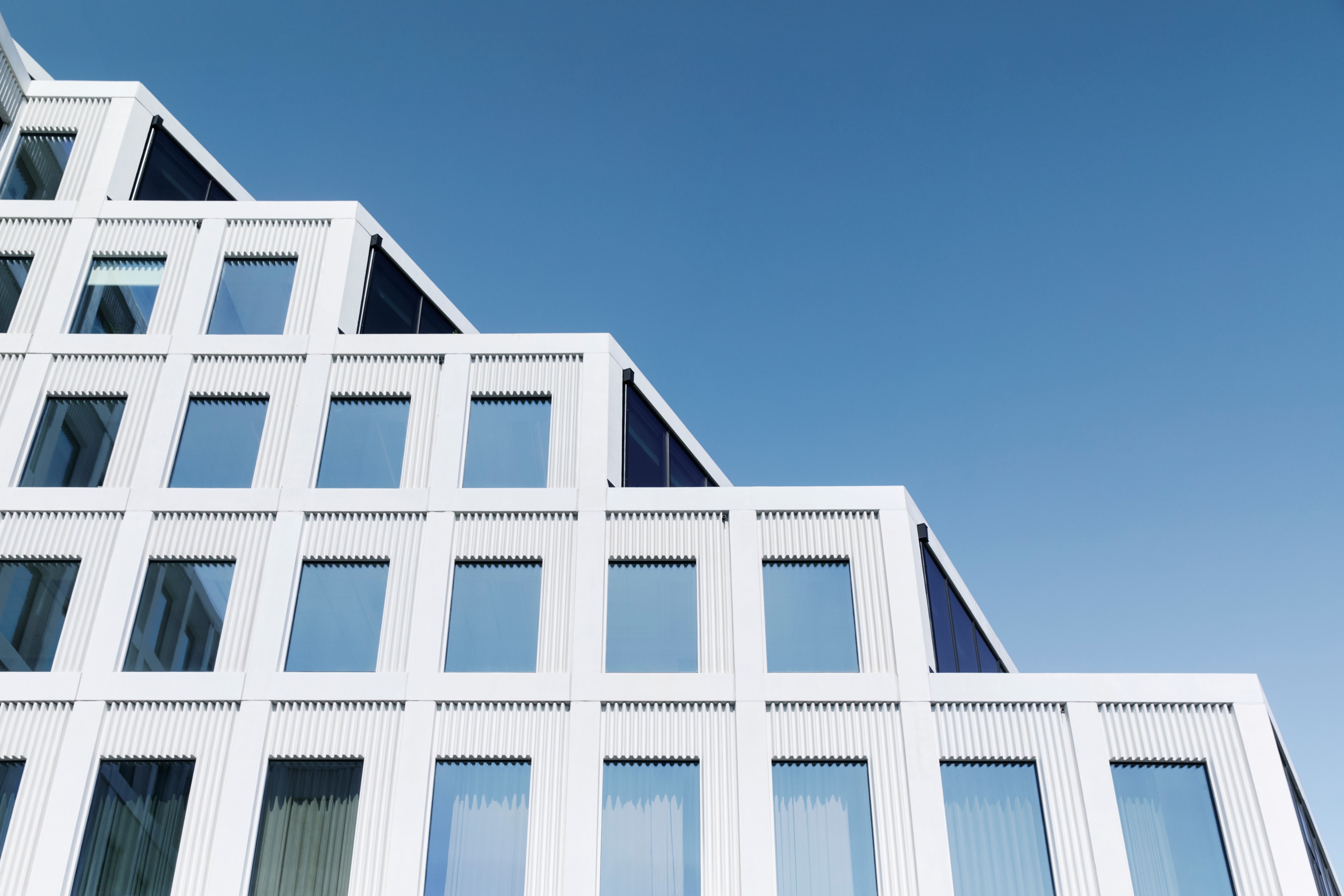 Modern white stepped building with large windows against a clear blue sky.