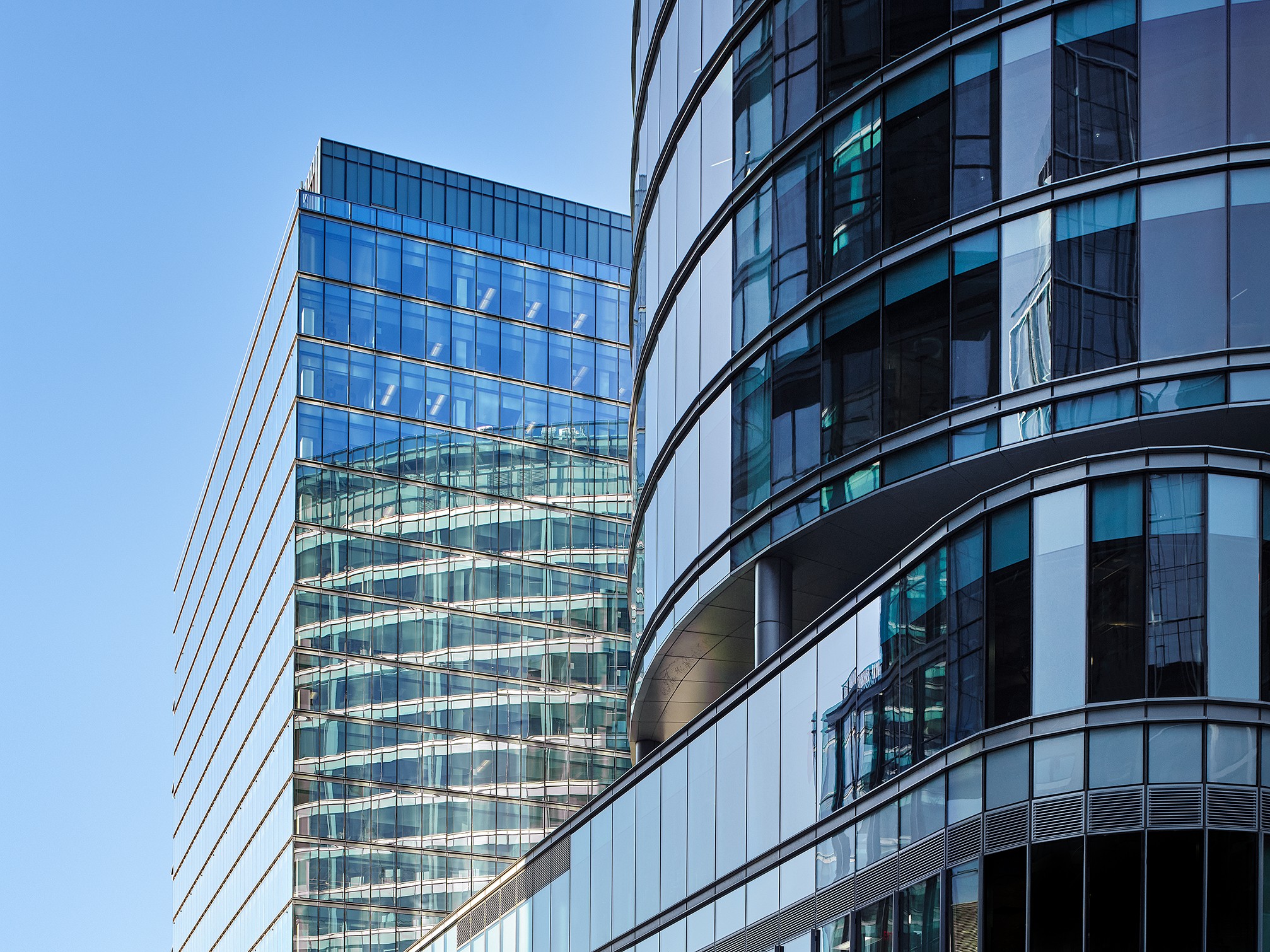 Modern glass office buildings with reflections under a clear blue sky.