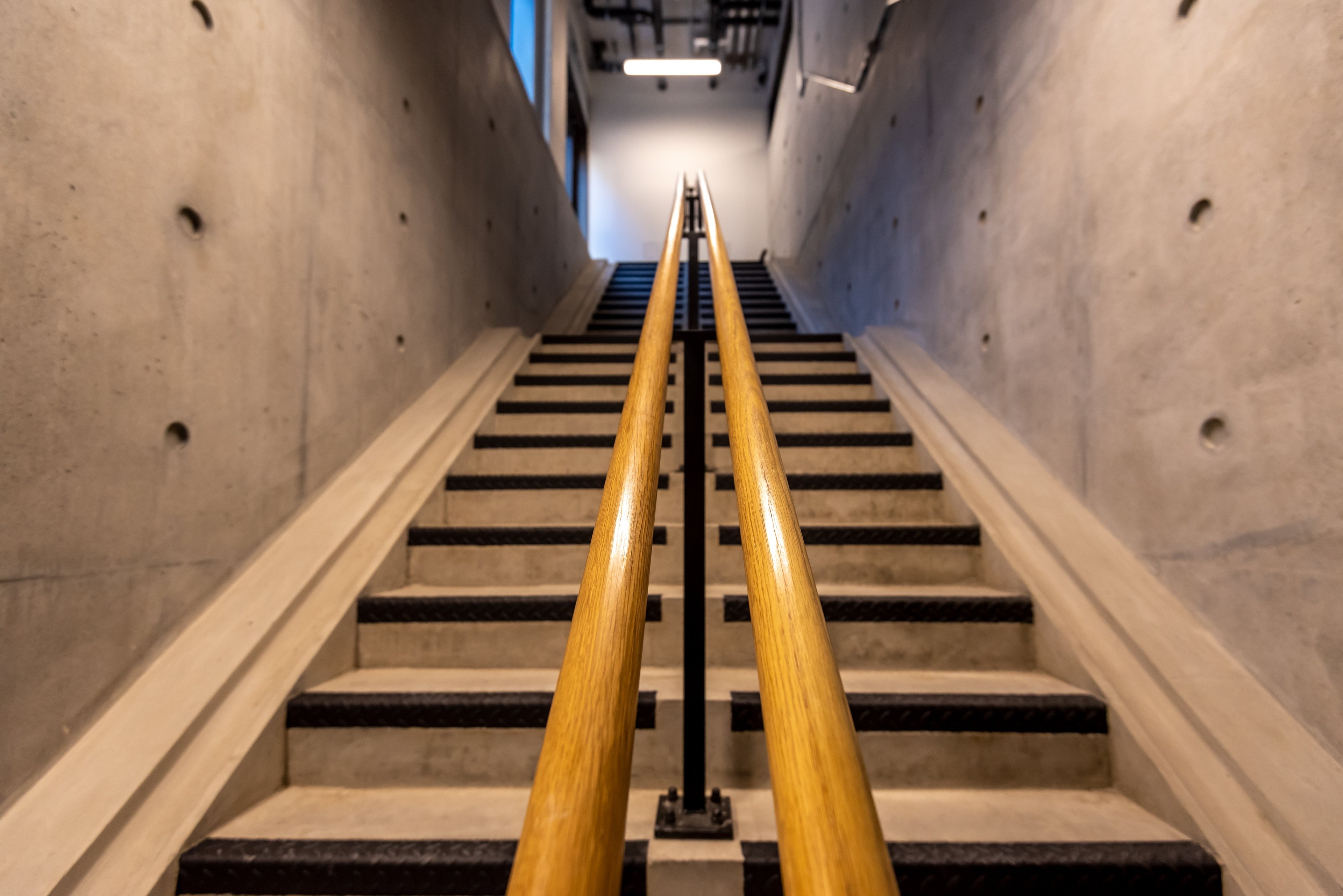 Concrete staircase with dual wooden handrails in a modern, industrial-style building.