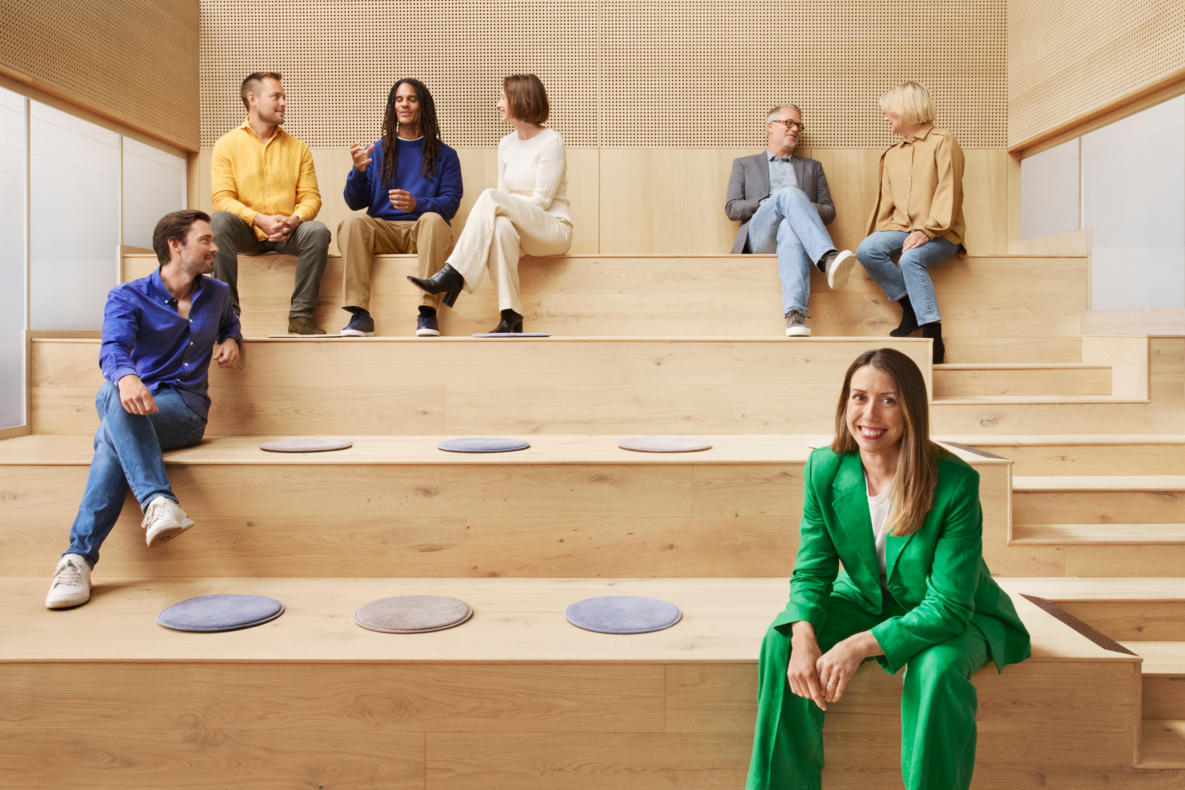 Group of people in casual and business attire sitting on wooden tiered seating in a modern room.