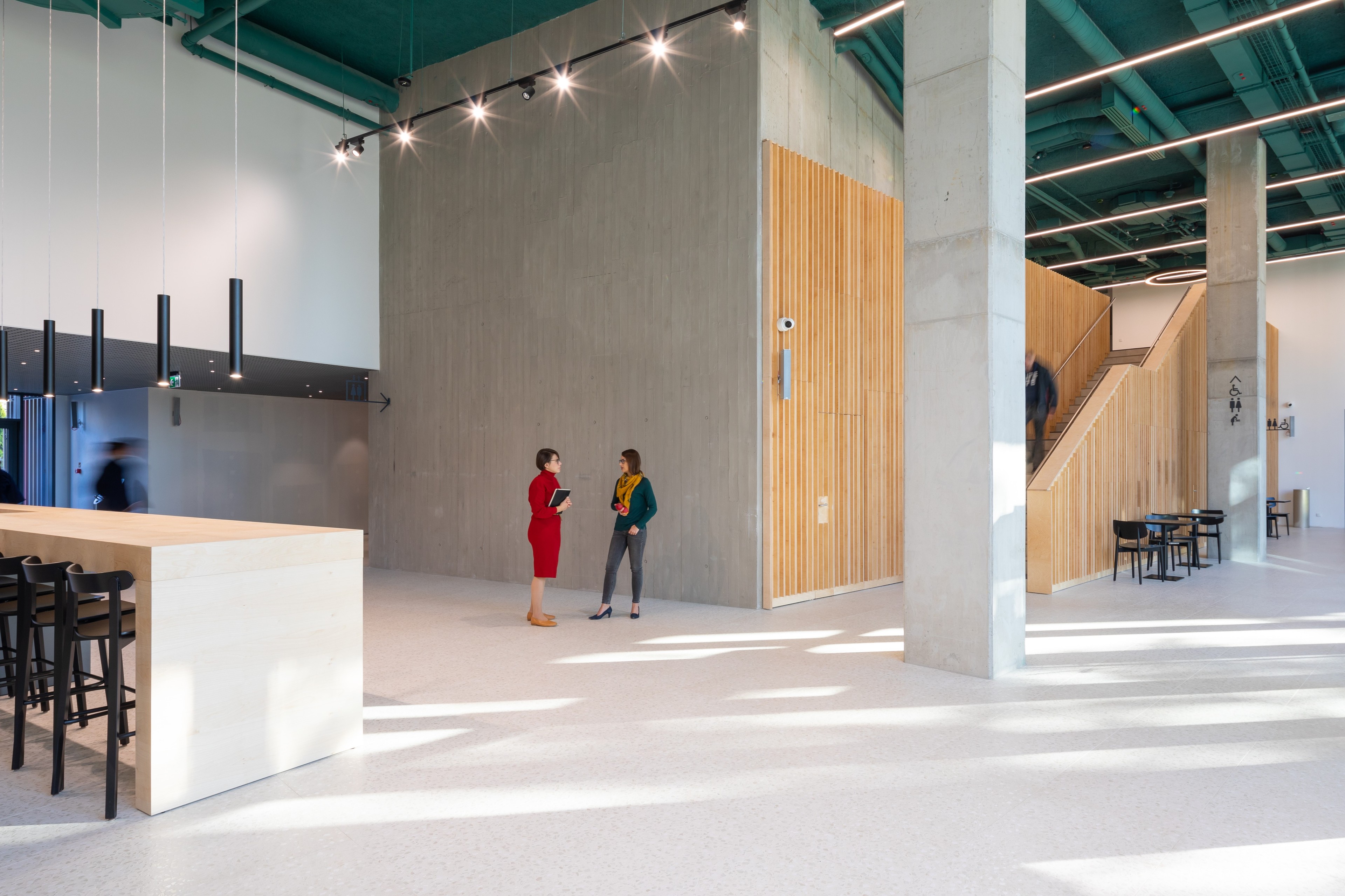Modern office interior with two people conversing, featuring wooden accents and sleek design.