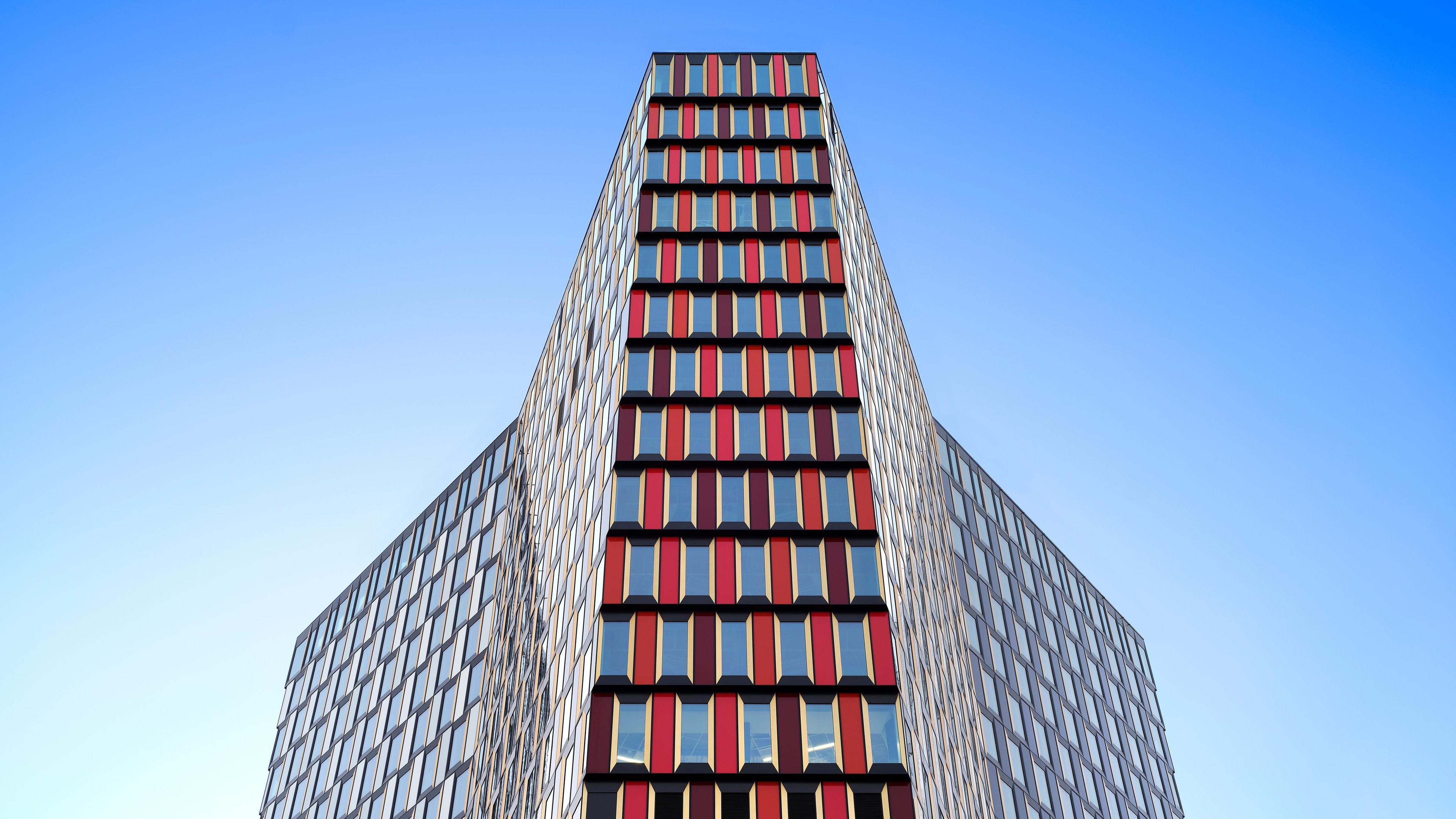 Modern glass office building with a unique geometric facade against a clear blue sky.