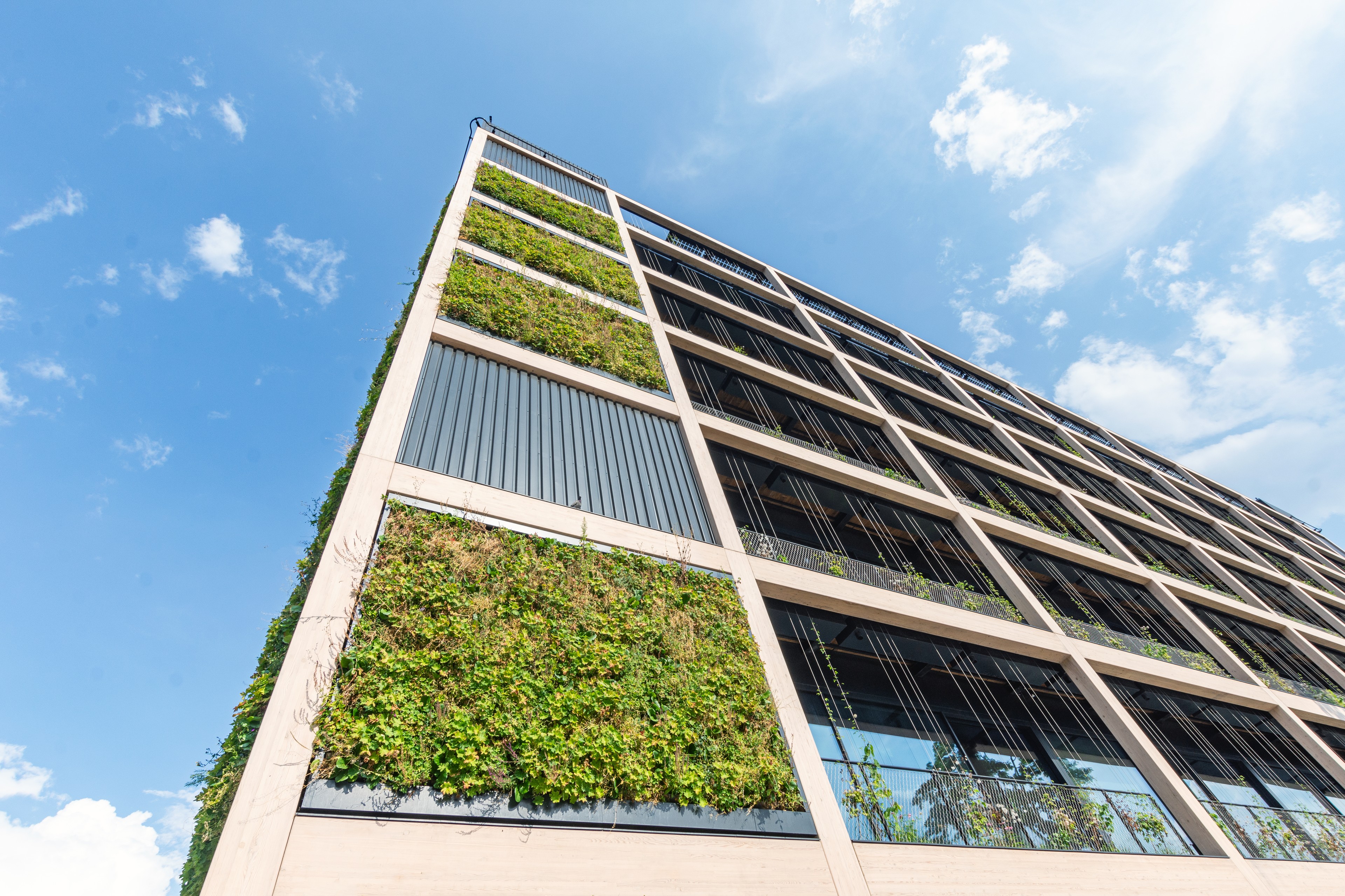 Modern building with vertical green gardens, blue sky, and clouds in the background.