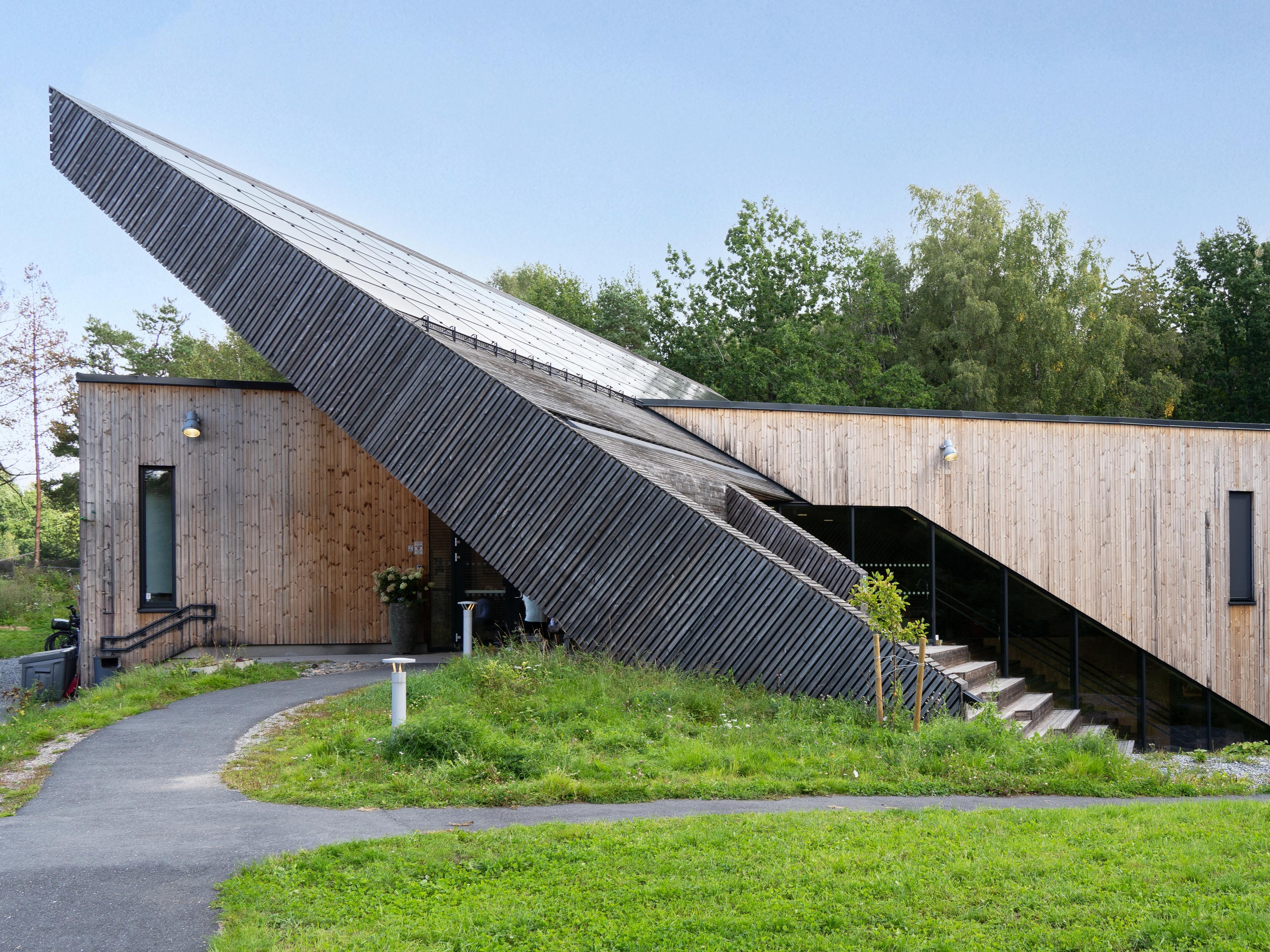 Modern wooden house with a sharp angled roof and lush green surroundings.