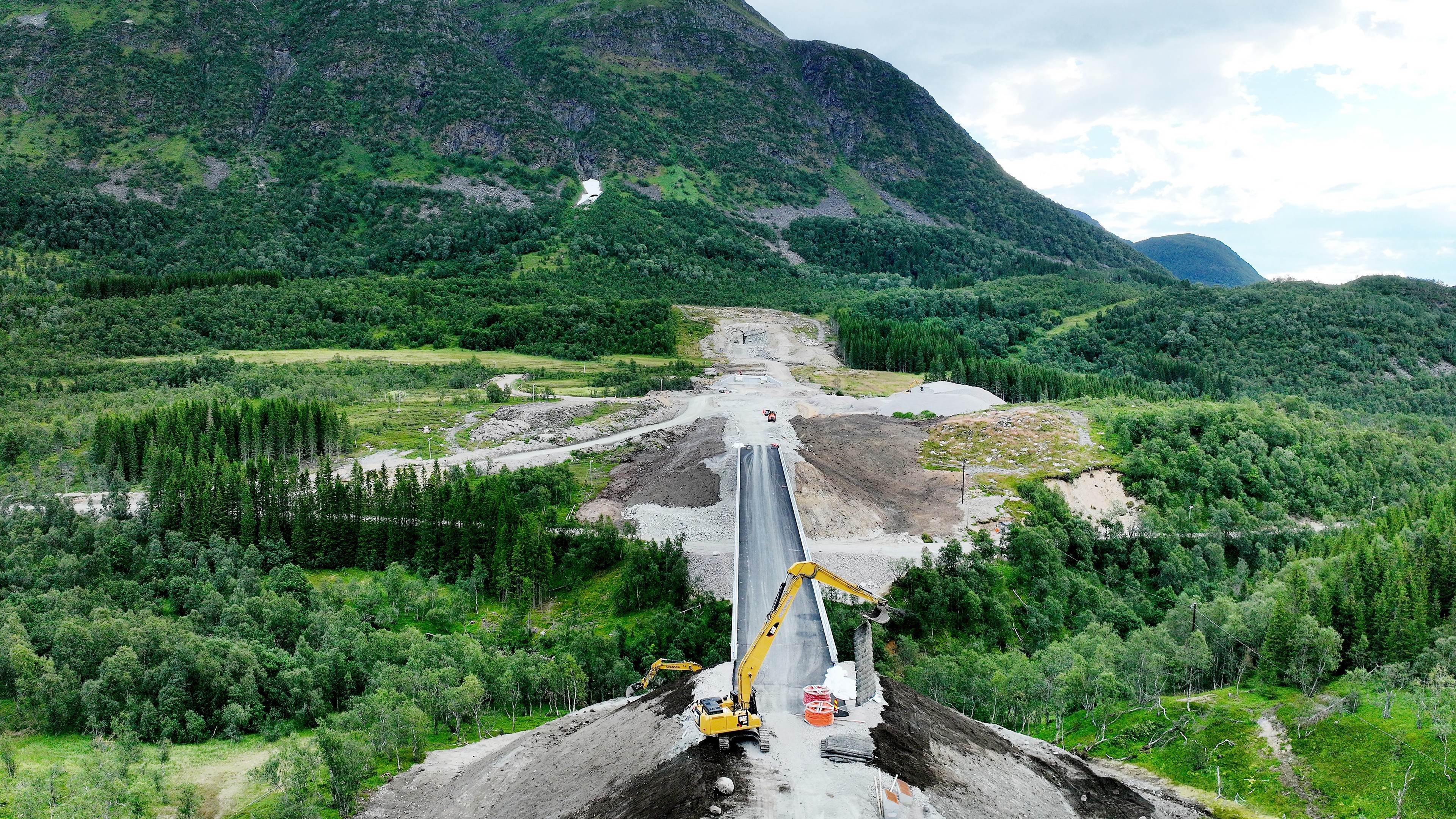 Construction of a new road bridge in a green mountainous landscape with heavy machinery.