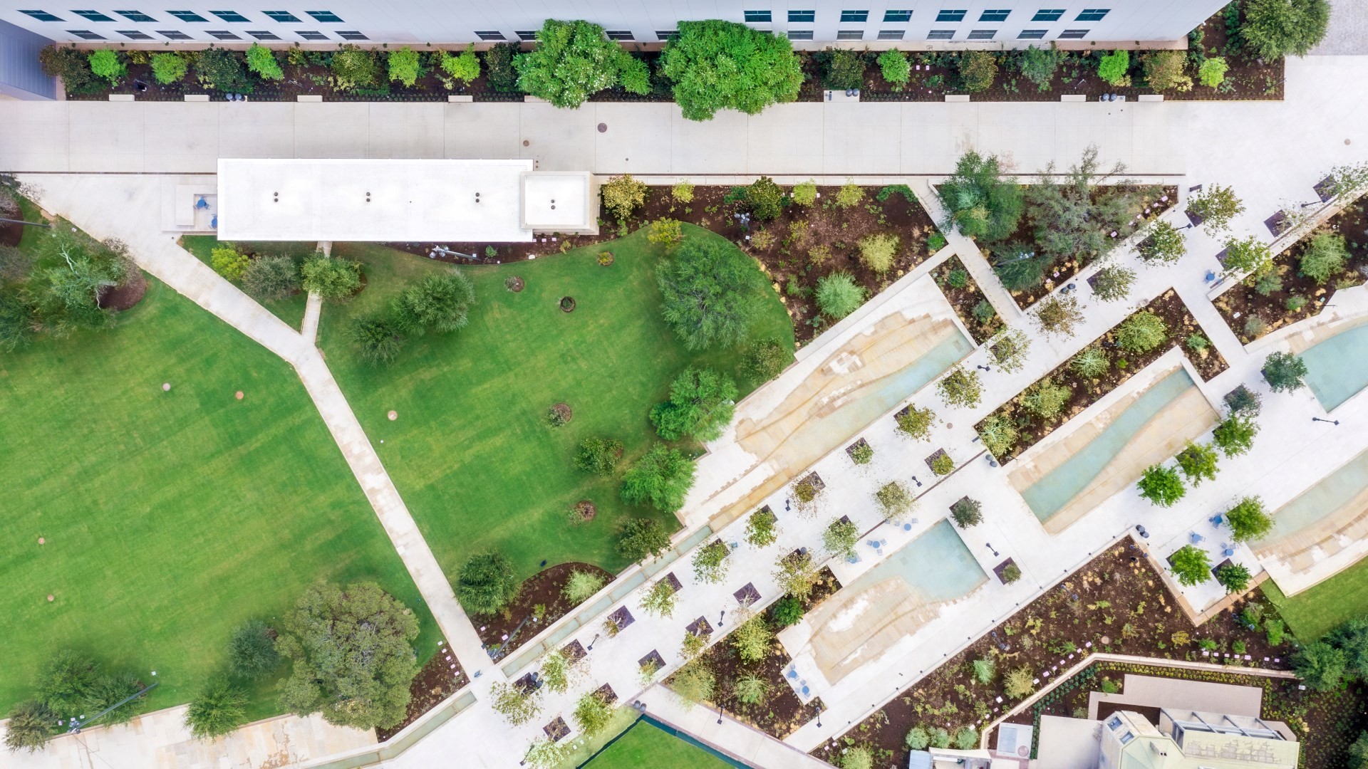 Aerial view of a landscaped urban park with green lawns, pathways, and water features.