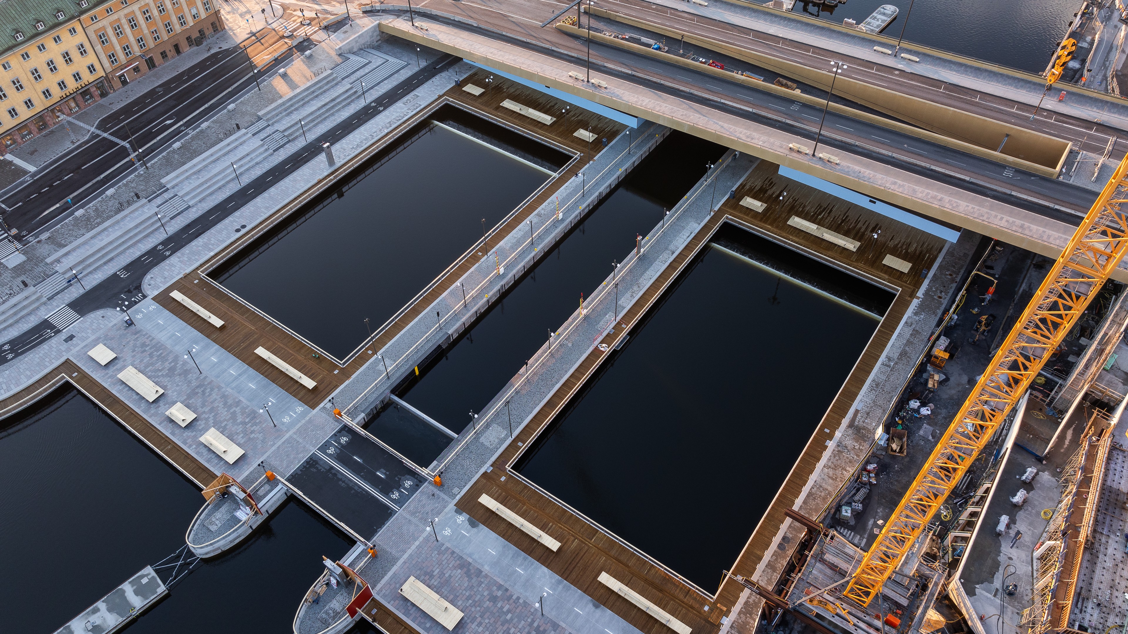 Aerial view of modern docks beneath a bridge, featuring geometric design and construction cranes.