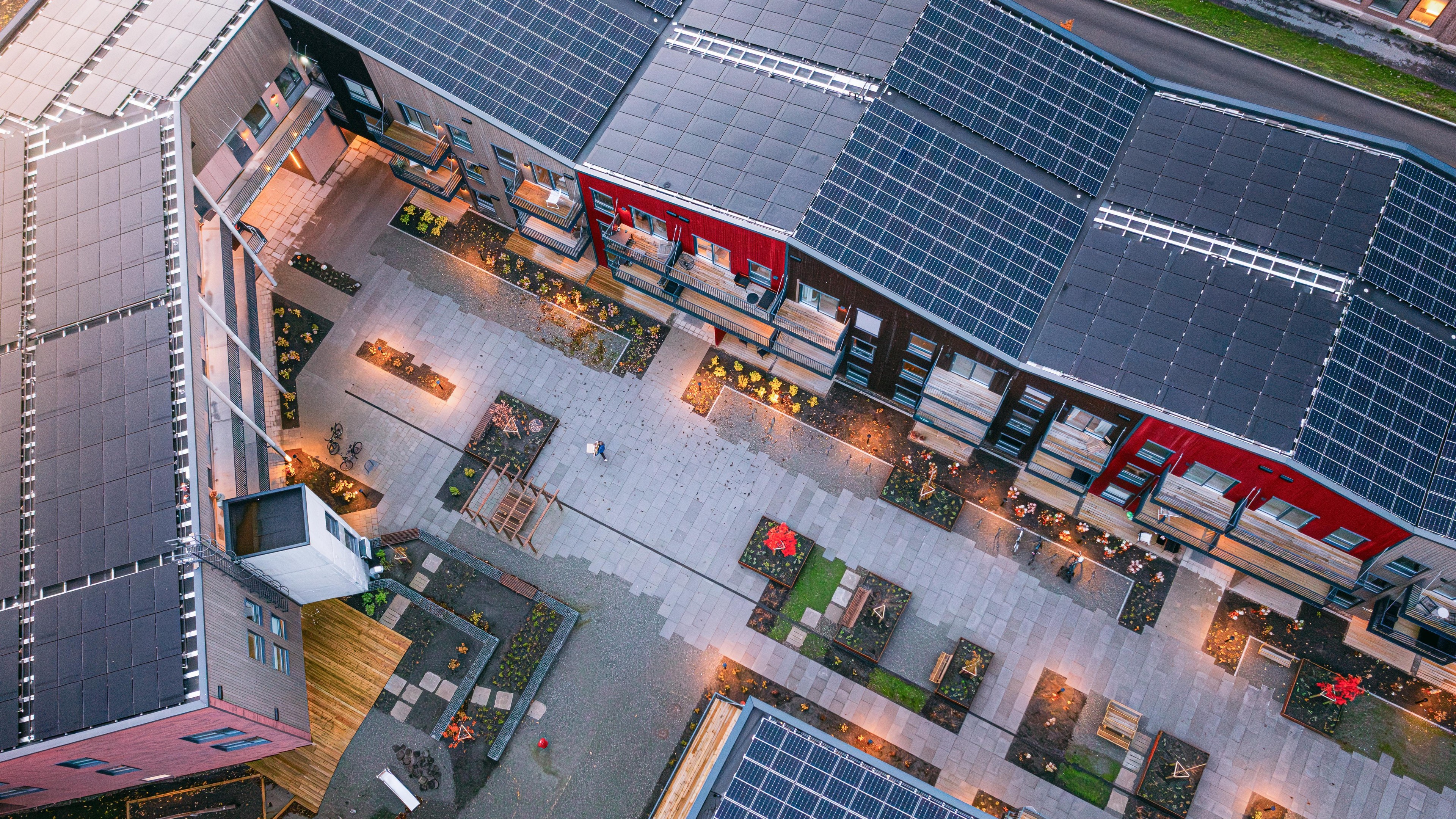 Aerial view of modern buildings with solar panels, featuring landscaped courtyards and walkways.