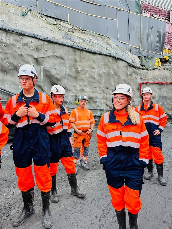 Gruppe av bygningsarbeidere i oransje sikkerhetsutstyr og hjelmer på en byggeplass.