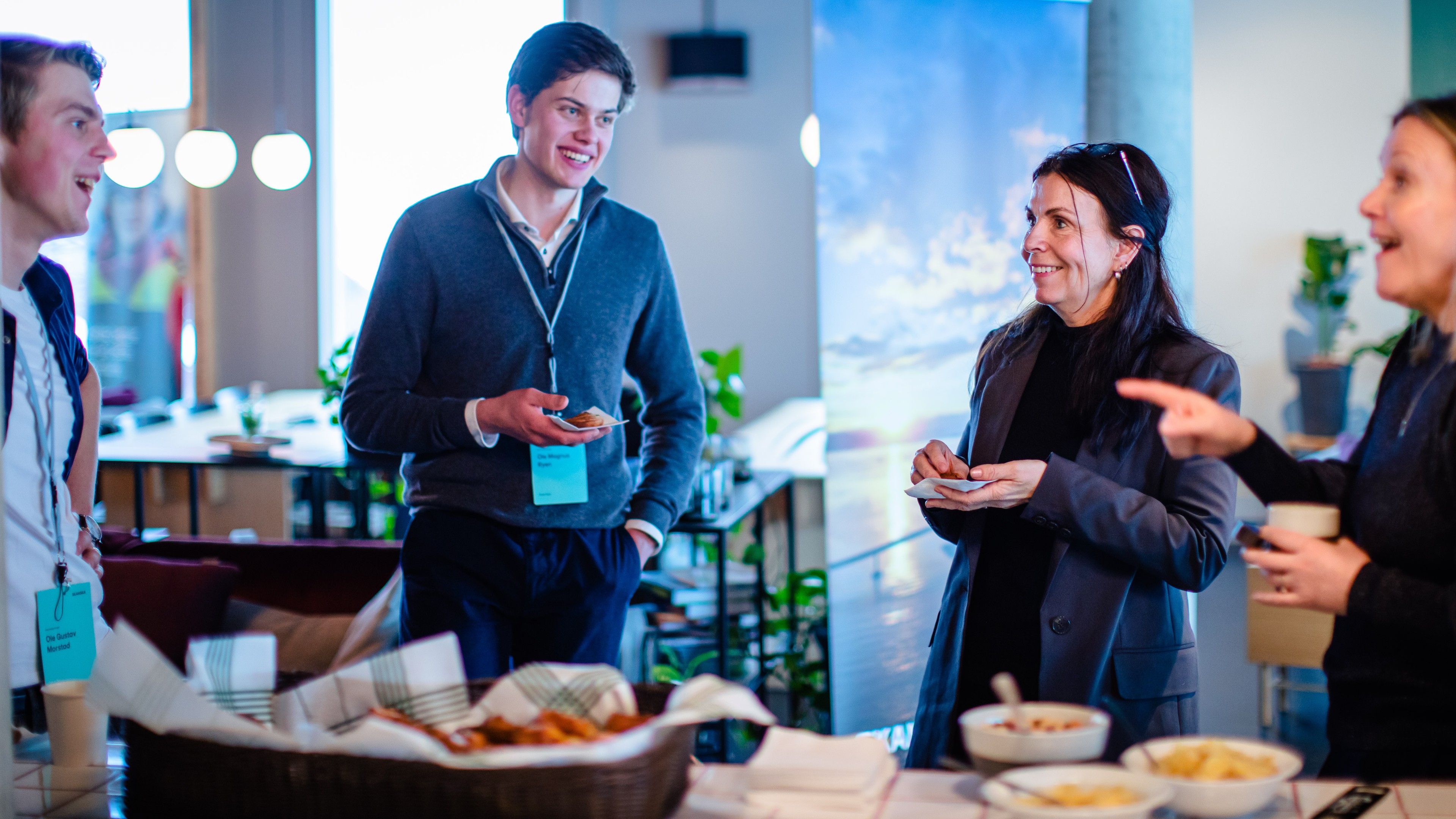 Networking event with professionals enjoying snacks and coffee Fagpersoner som nettverker og spiser snacks under et uformelt kontormøte eller arrangement.