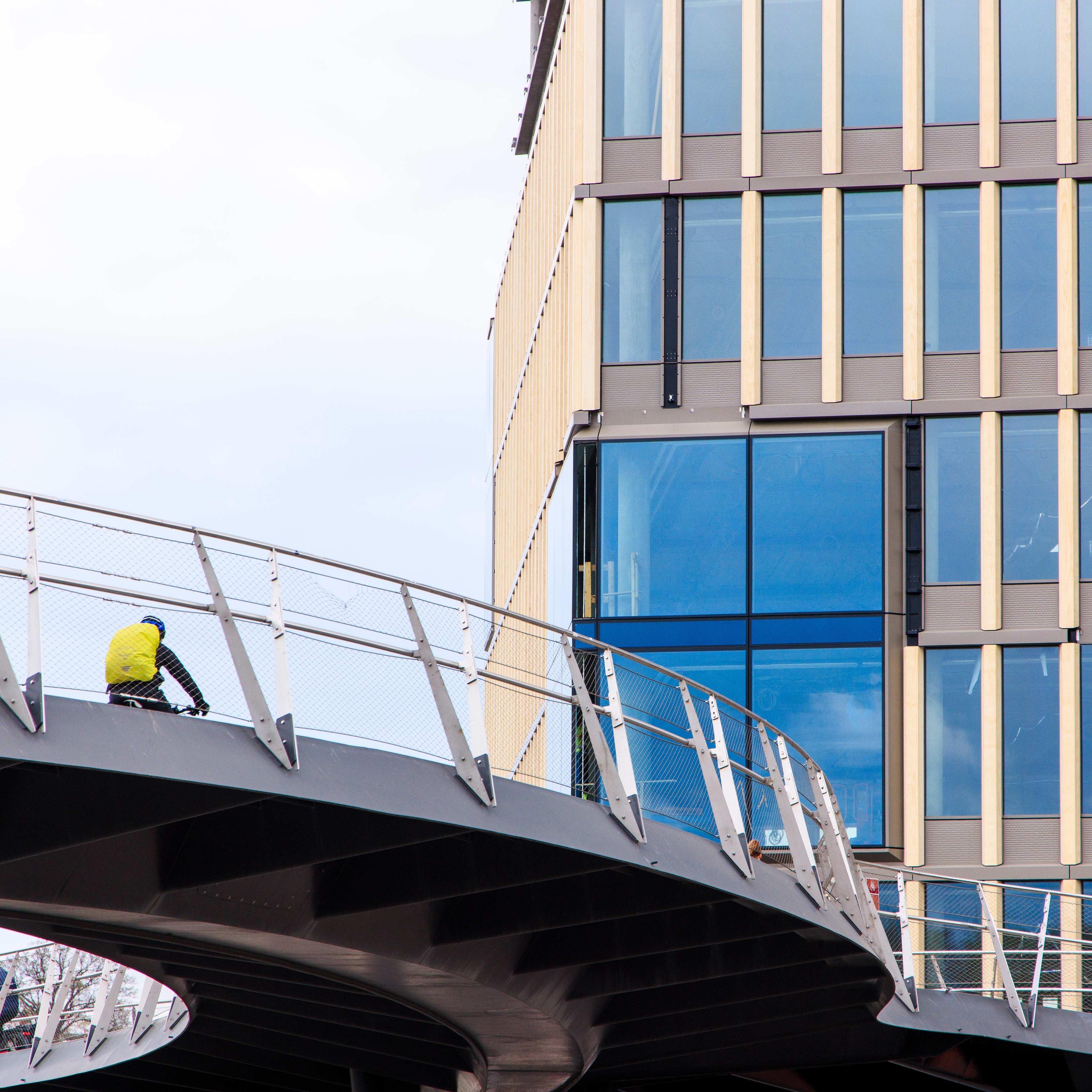 Sykkelritt på en moderne bro nær en glassbygning, med elegant arkitektur og bydesign.