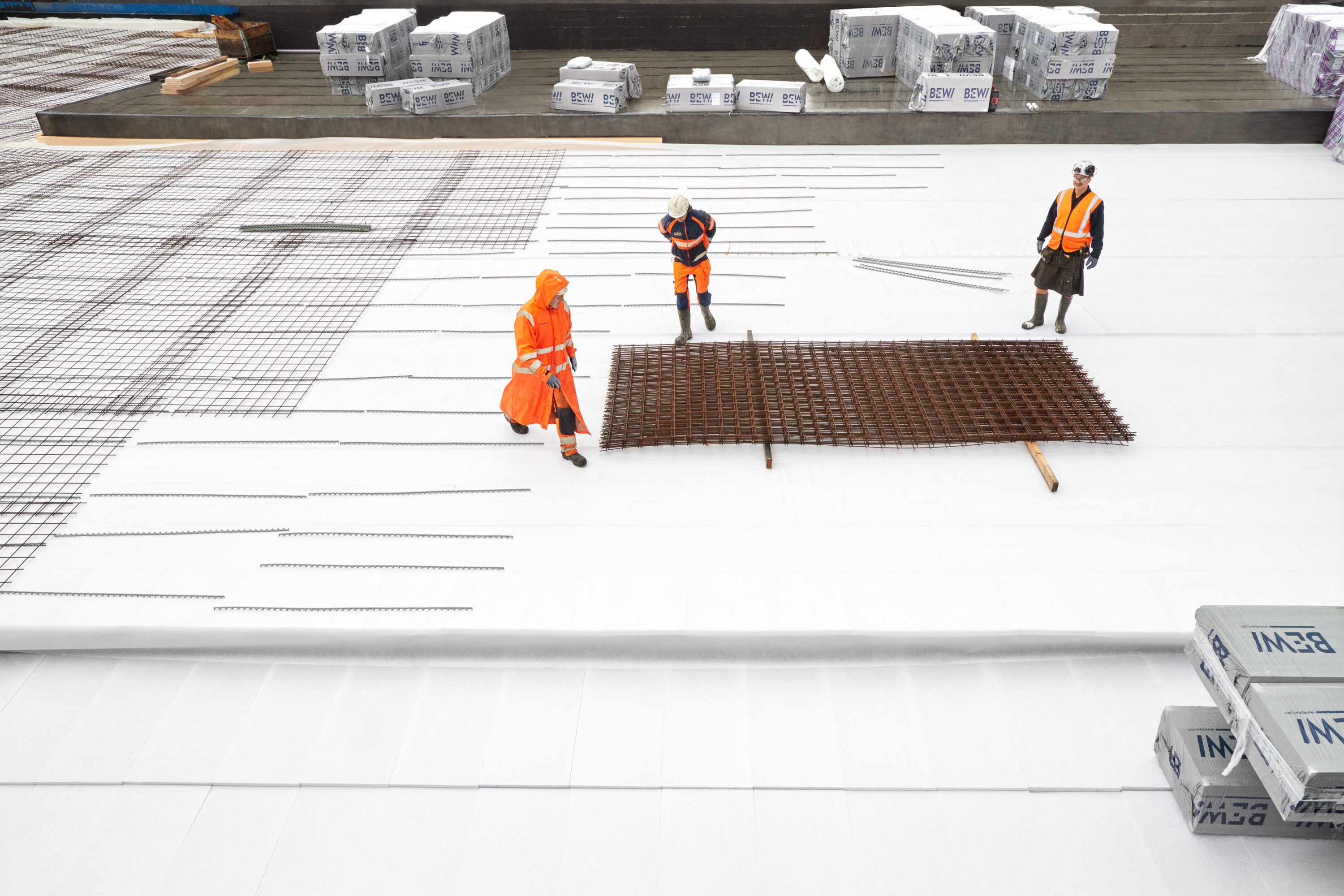 Bygningsarbeidere ordner stålarmering på en stor, isolert grunnplate på en byggeplass.