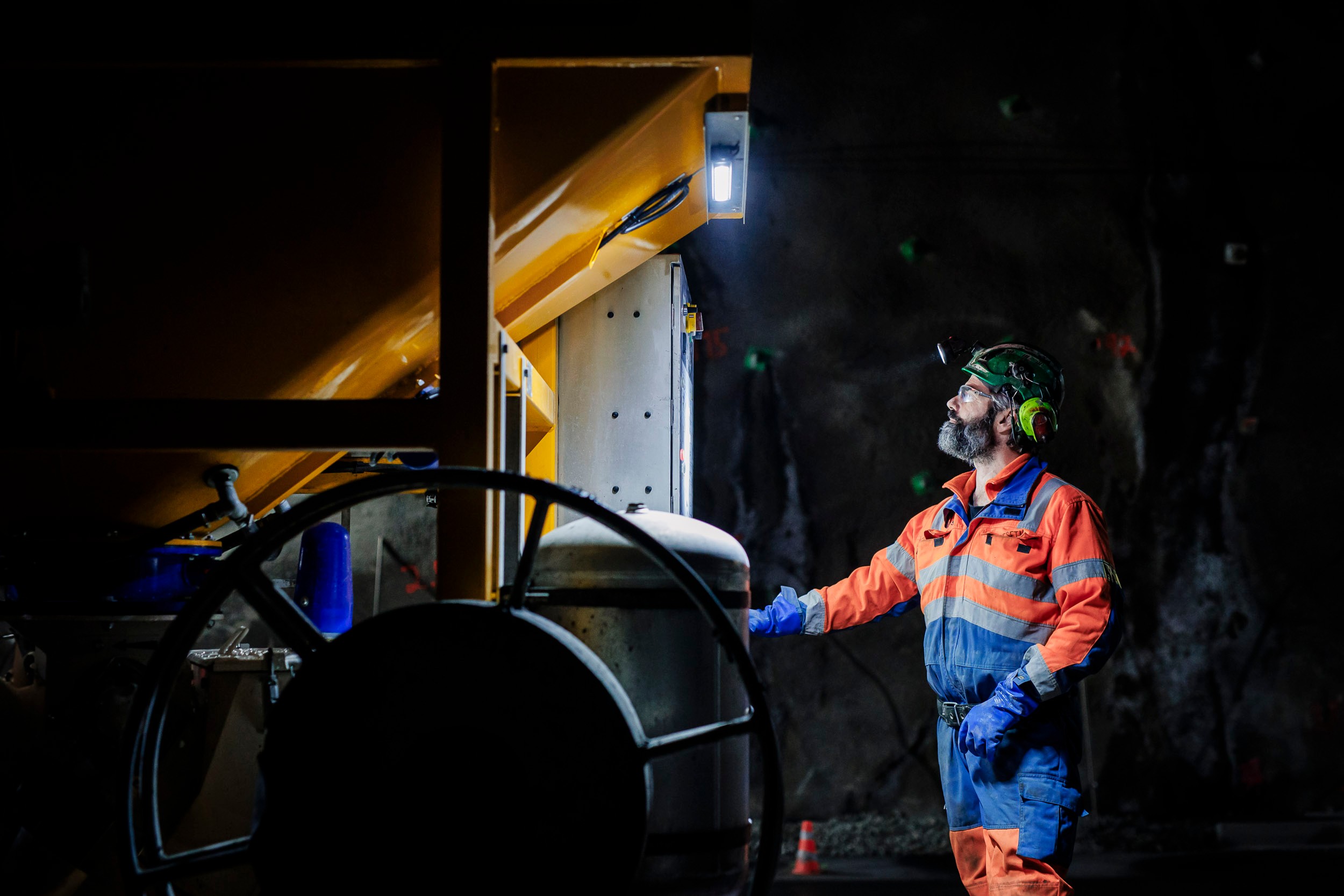 Underground Worker in Safety Gear Operating Heavy Machinery En arbeider i verneutstyr betjener maskineri i et svakt opplyst industrielt miljø.