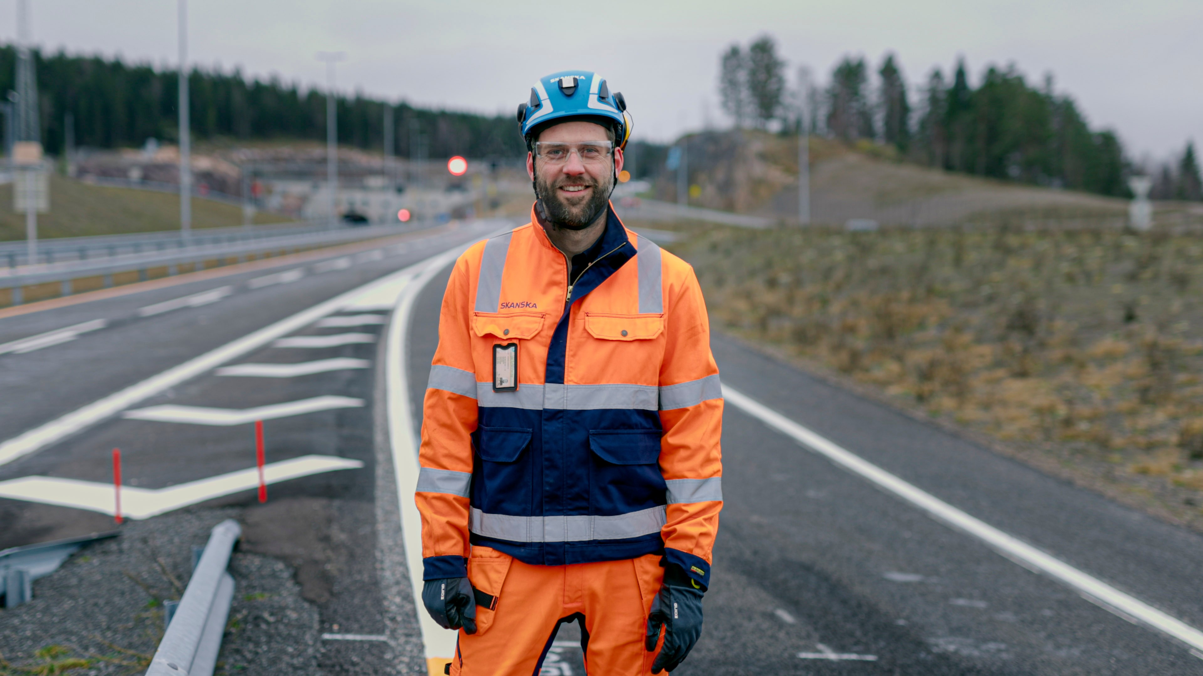 En bygningsarbeider i synlighetsutstyr står på en nylagt vei nær et landlig område.