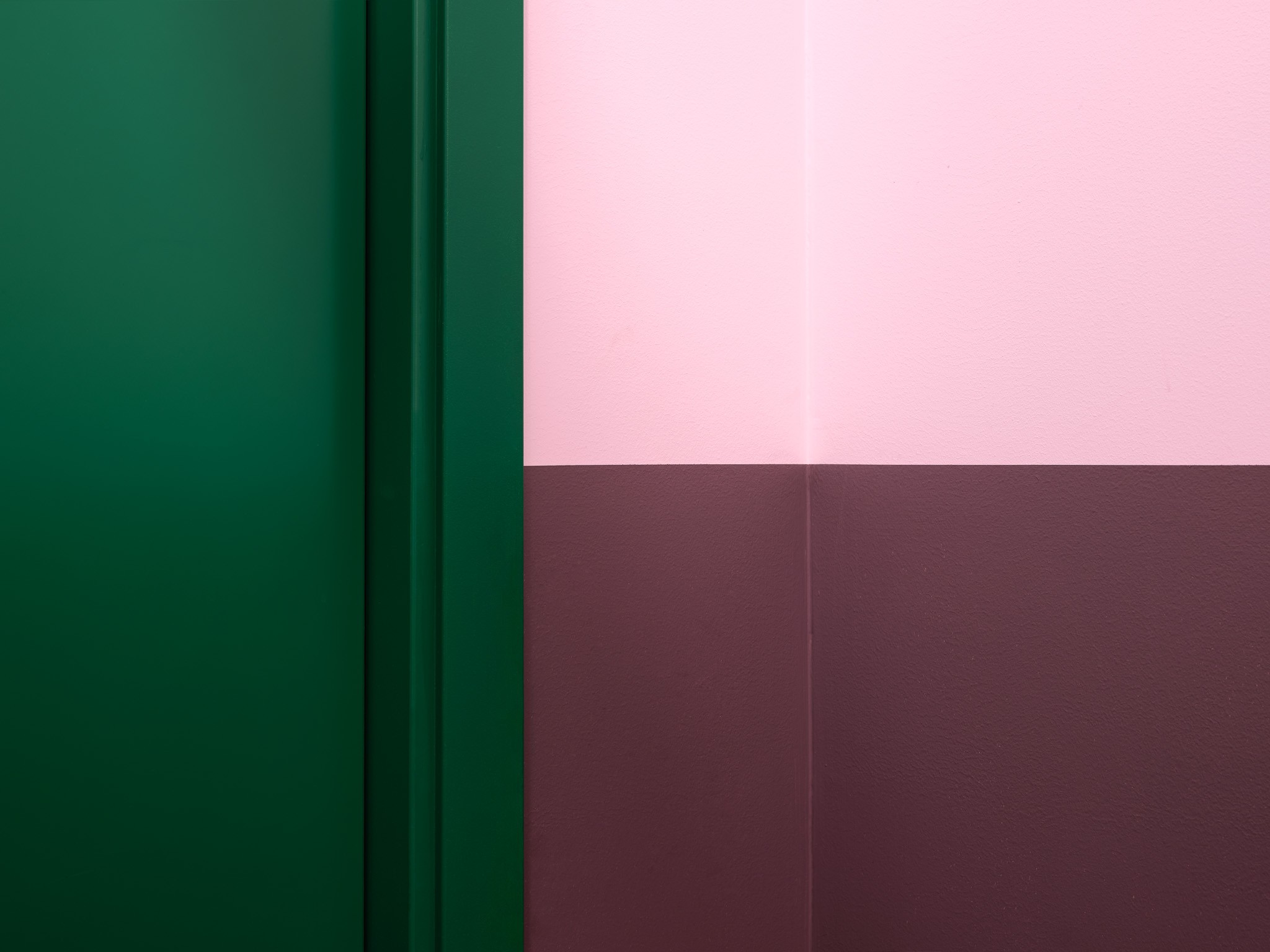 Hjørne med en grønn dør og en vegg malt i rosa og brun, som viser kontrasterende farger.
