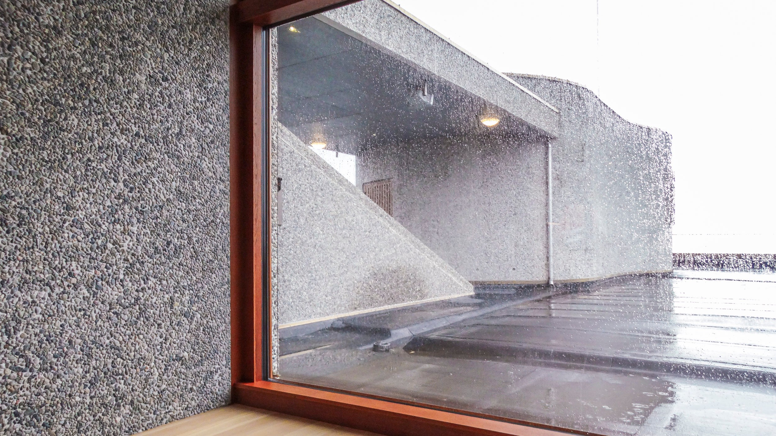 Utsikt gjennom et regnvått vindu som viser en betongbygning med moderne design.