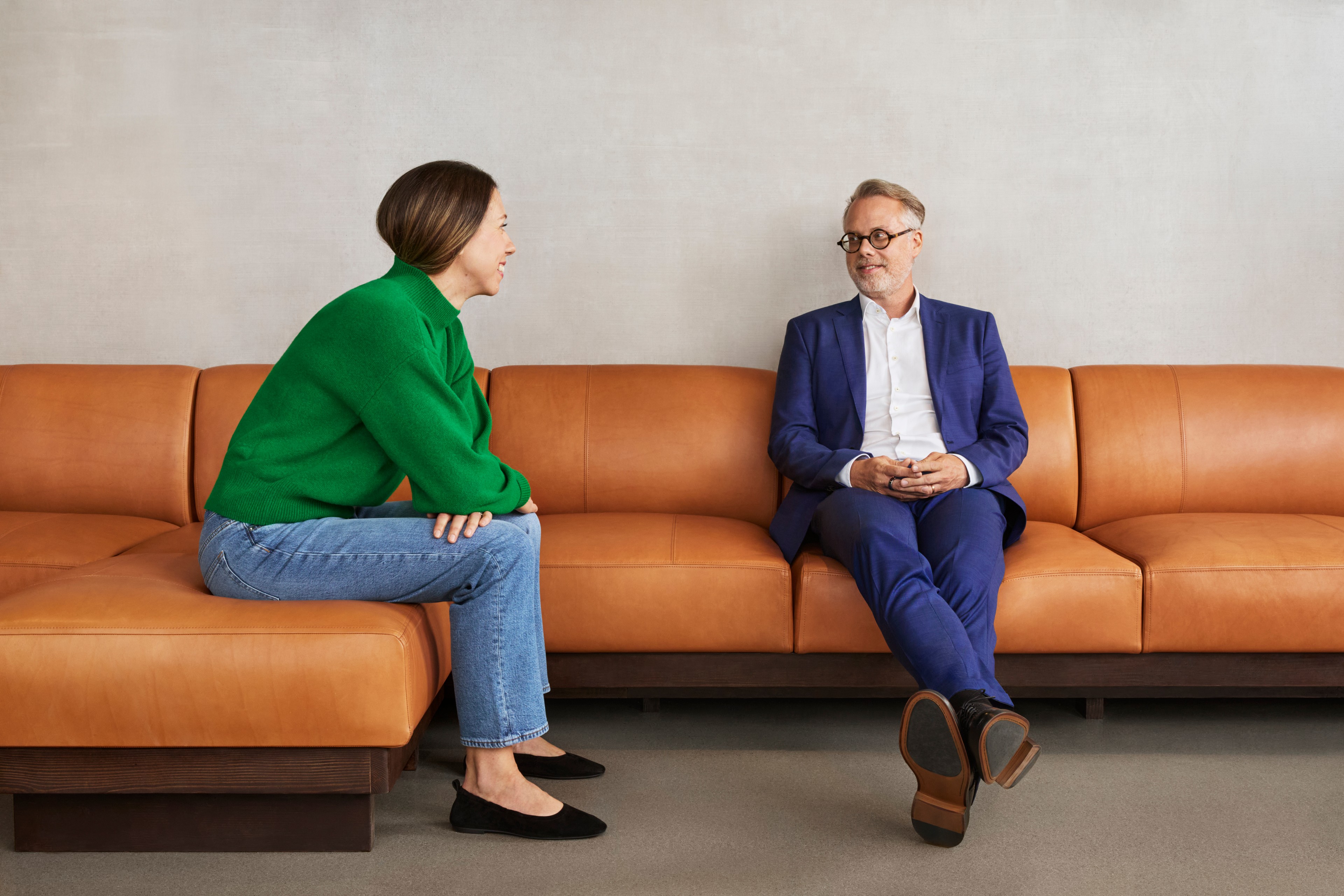 To personer engasjert i en seriøs samtale mens de sitter på en moderne skinnsofa.