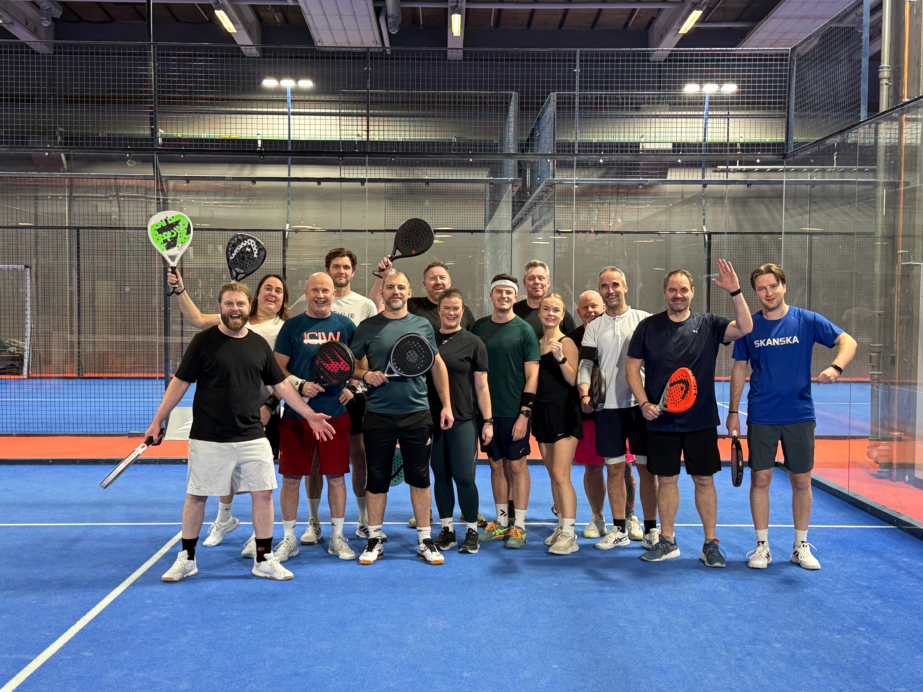 Gruppe mennesker poserer med padelracketer på en innendørs bane, viser sportsentusiasme.