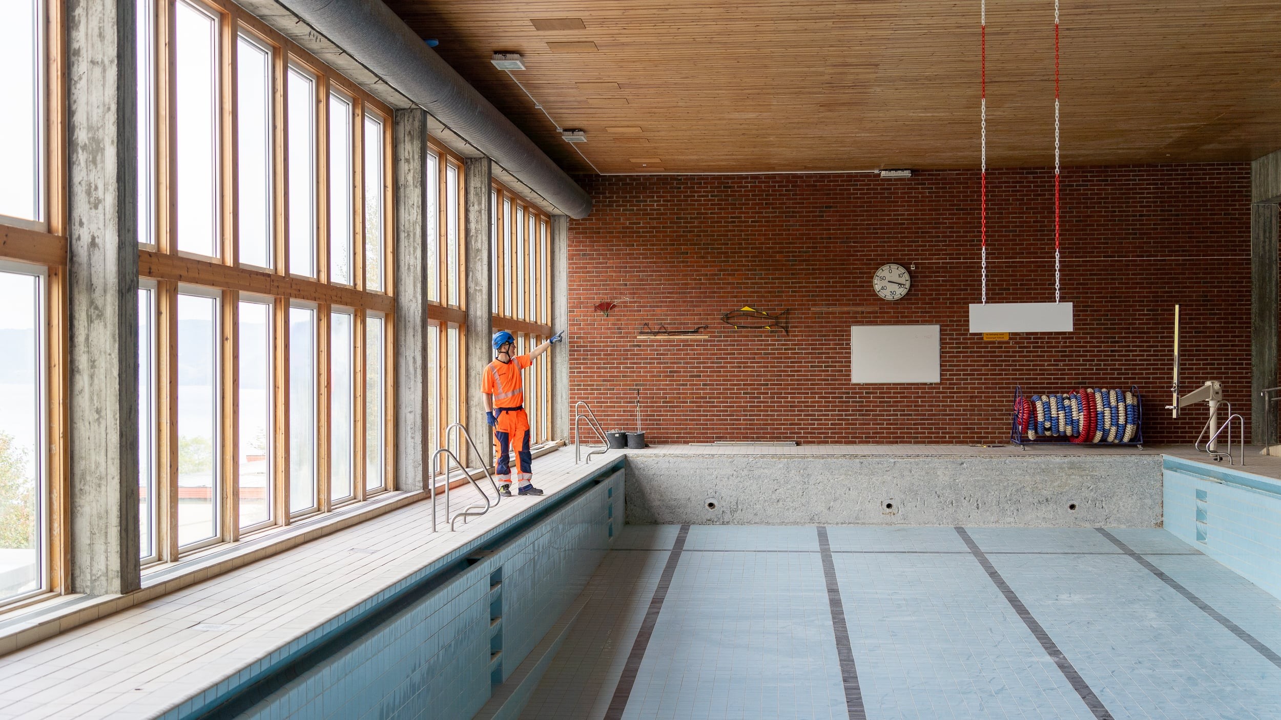 Empty Pool Inspection in Bright Industrial Setting En bygningsarbeider i synlighetsklær står nær store betongstrukturer på en arbeidsplass.
