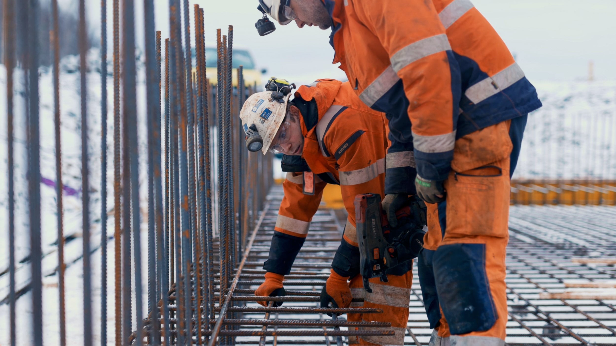 Construction workers installing steel reinforcement bars on site Bygningsarbeidere i oransje verneutstyr som installerer stål armeringsjern på en byggeplass.