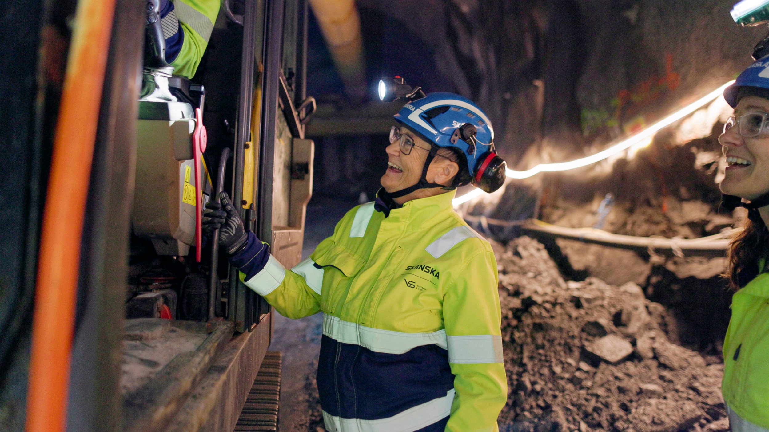 Arbeider iført verneutstyr som betjener maskineri inne i en underjordisk gruvetunnel.