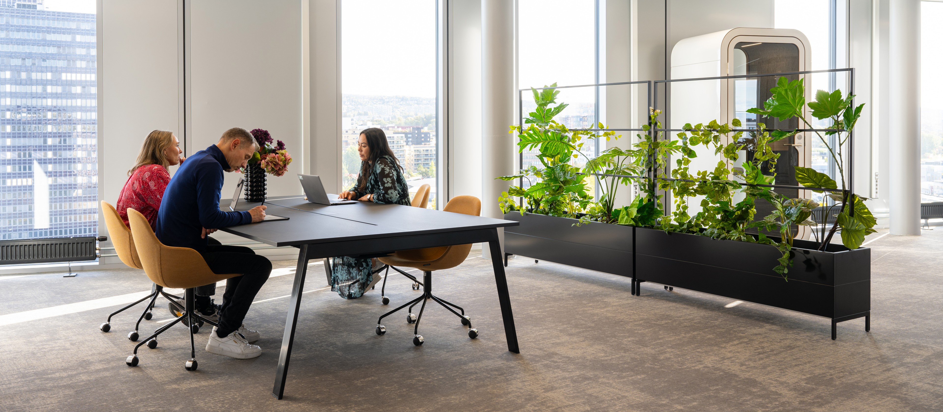 Moderne kontorlokale med inneplanter og møterom Moderne kontormøterom med tre personer, store vinduer og frodige innendørs planter.