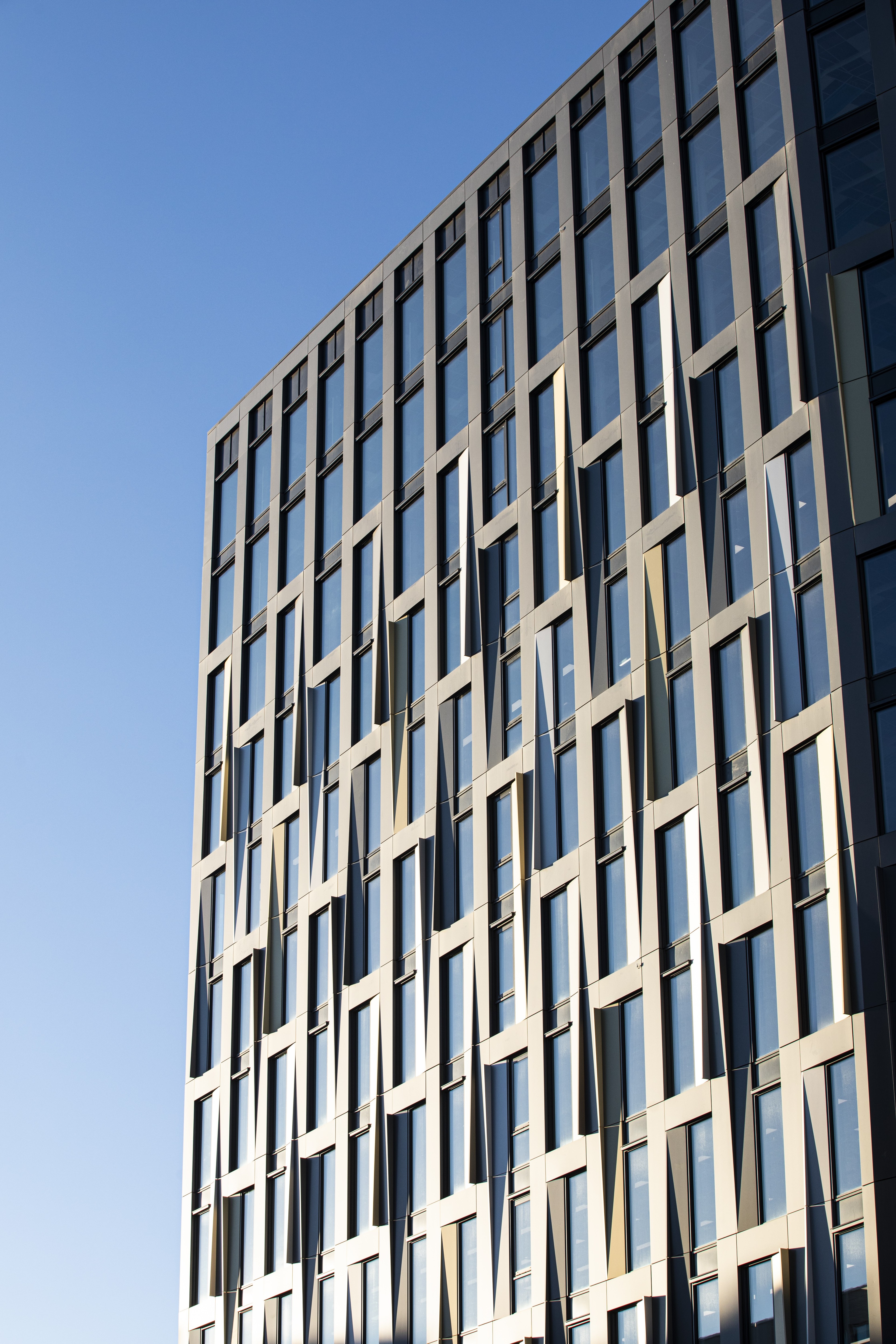 Moderne urban arkitektur med grønne områder og transport Moderne høyhus med geometriske vinduer mot en klar blå himmel.