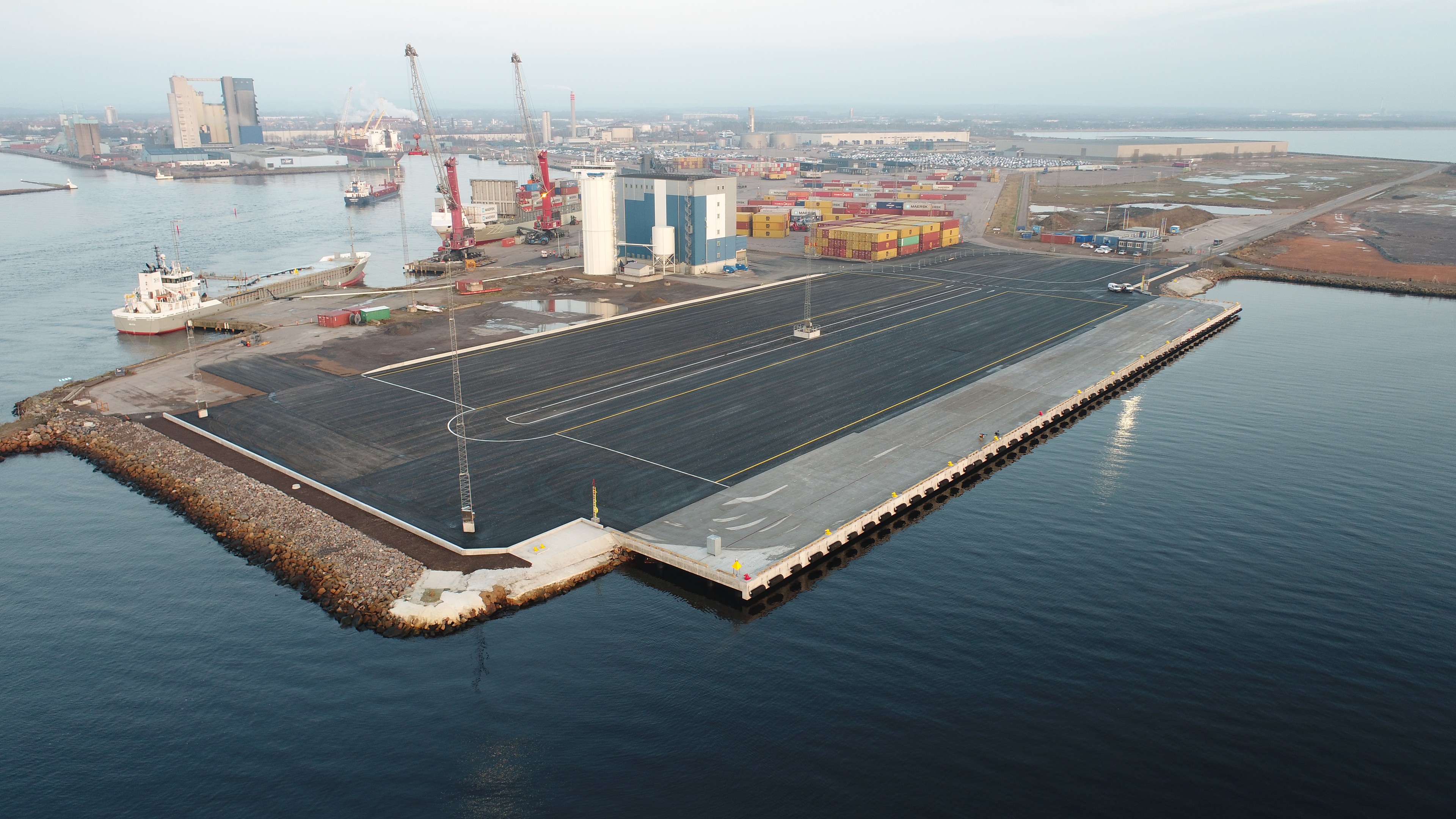 Saltkajens byggarbetsplats vid vattnet med kran och fartyg i sikte En byggkran på en plattform vid vattnet, med ett kryssningsfartyg och molnig himmel i bakgrunden.