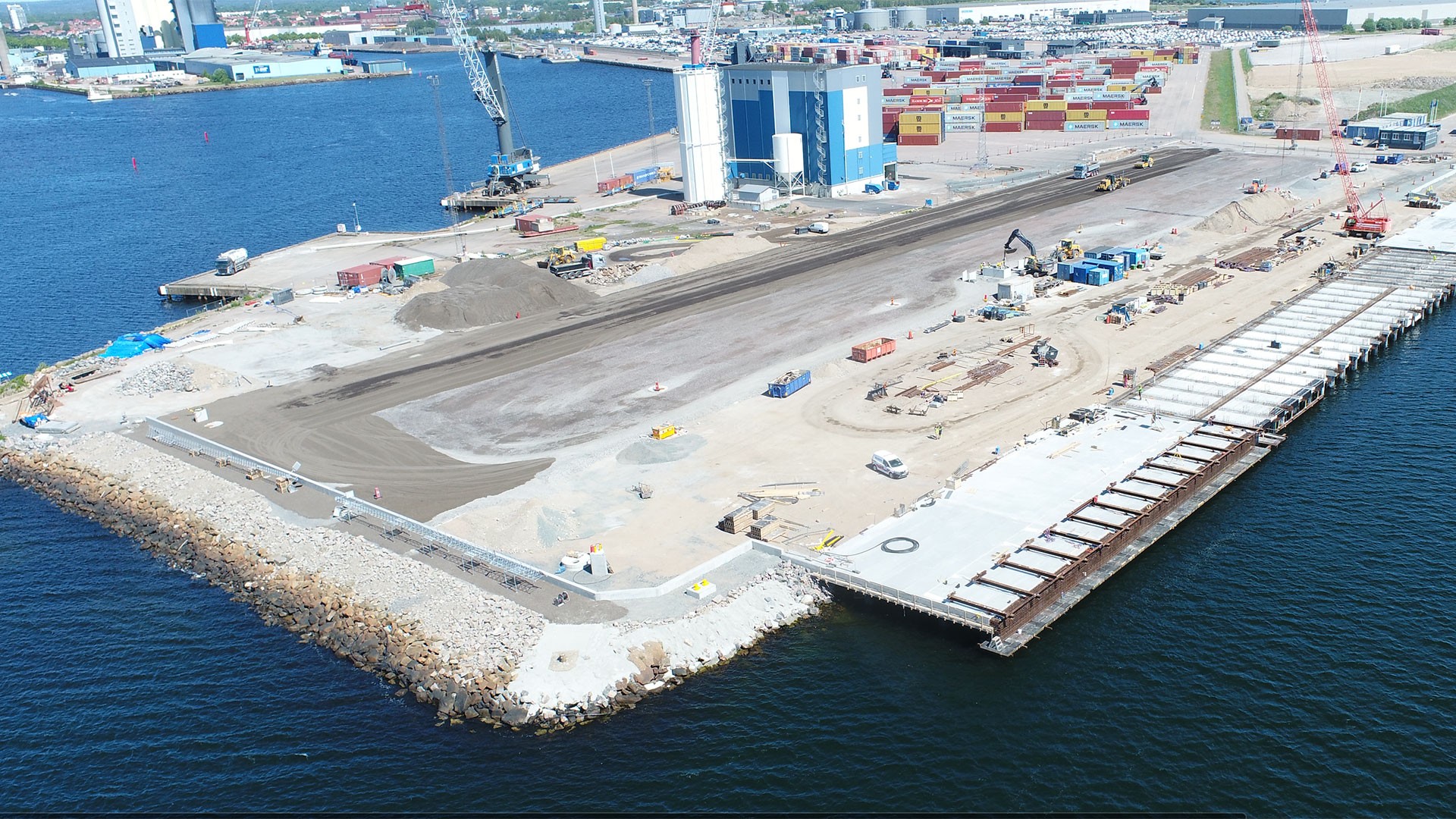 At Pier 800, Oceanhamnen, work is ongoing at the waterfront area. Aerial view of a coastal construction site with cranes and shipping containers by the sea.