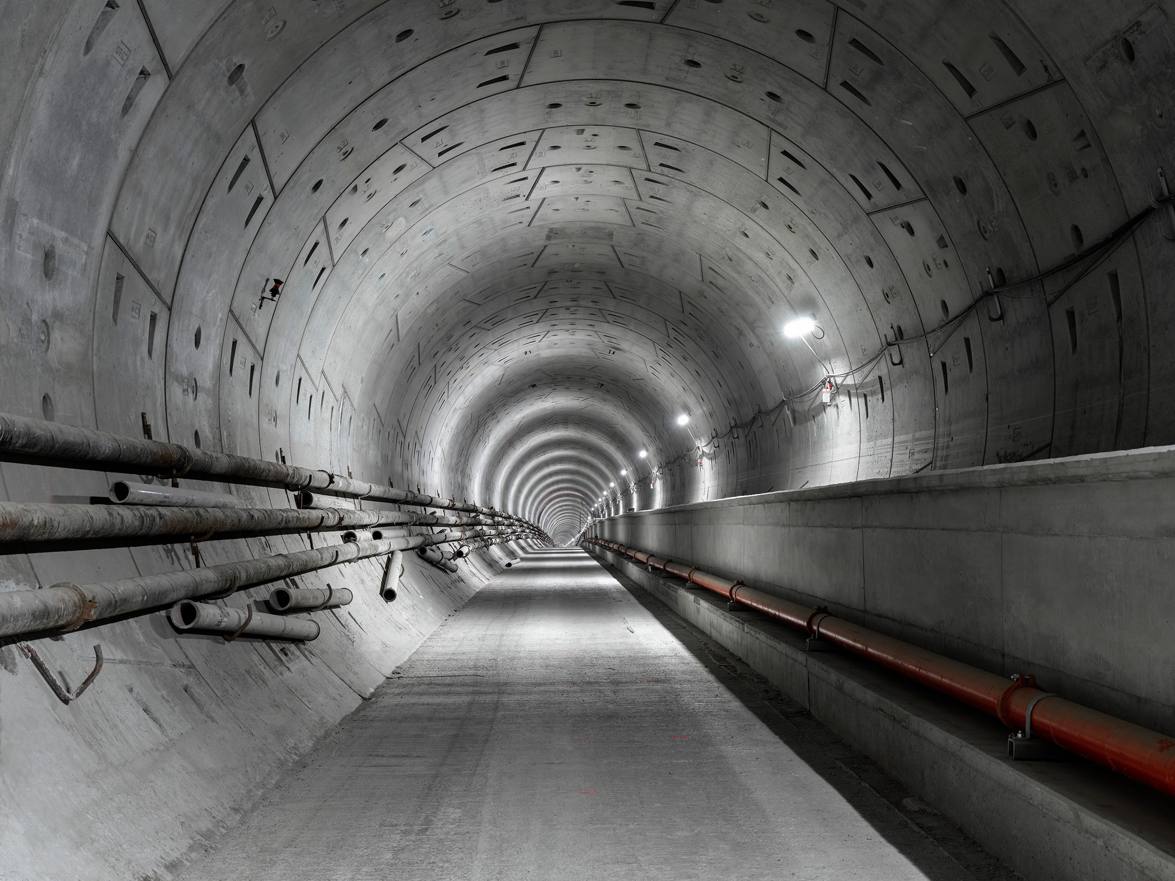 Modern underjordisk tunnel med belysning och rör En väl upplyst betongtunnel med rör längs de böjda väggarna, som sträcker sig in i fjärran.