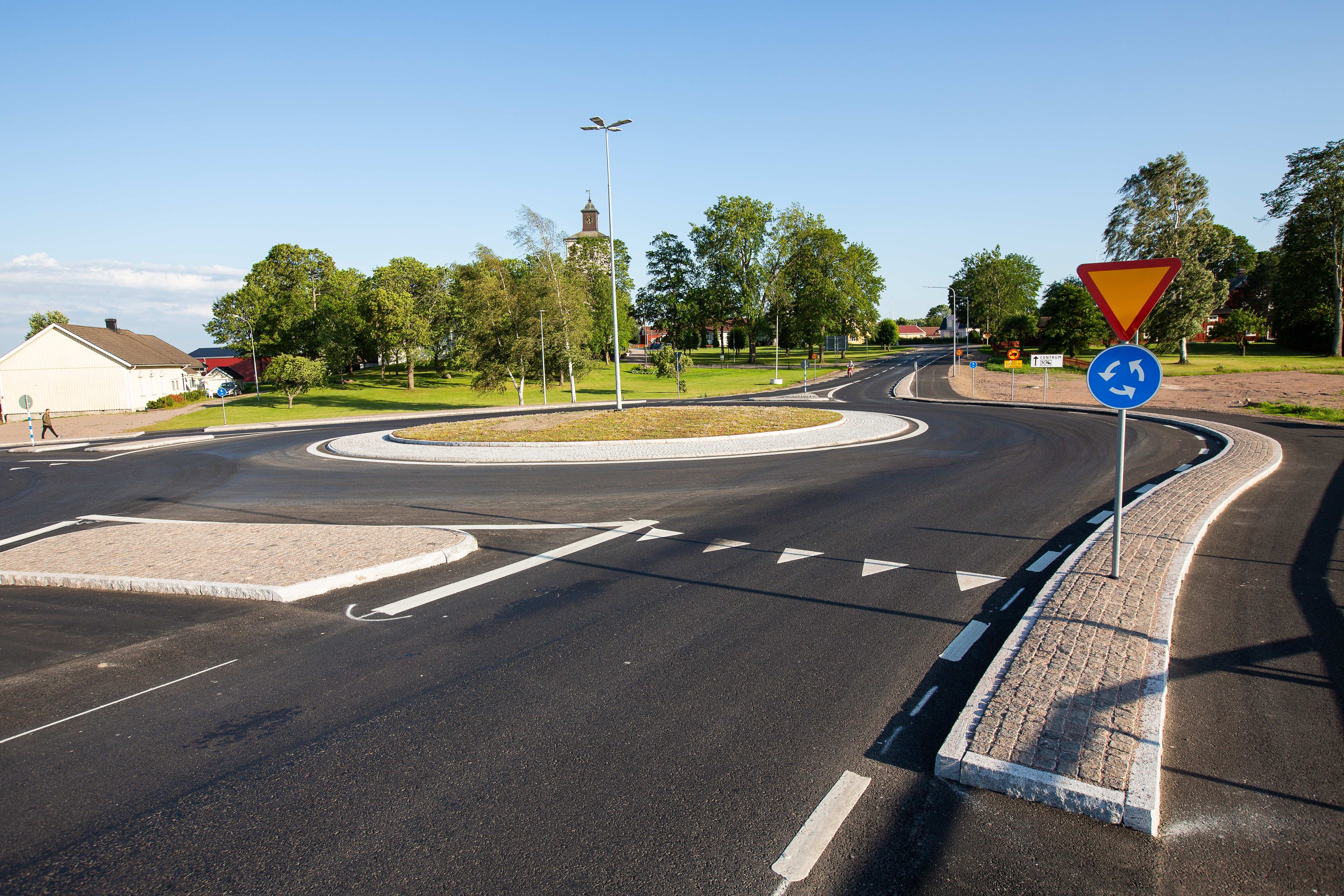 Modern rondelldesign i en naturskön stadsmiljö En modern rondell med tydliga vägmärken och vägmarkeringar, omgiven av frodig grönska och träd.