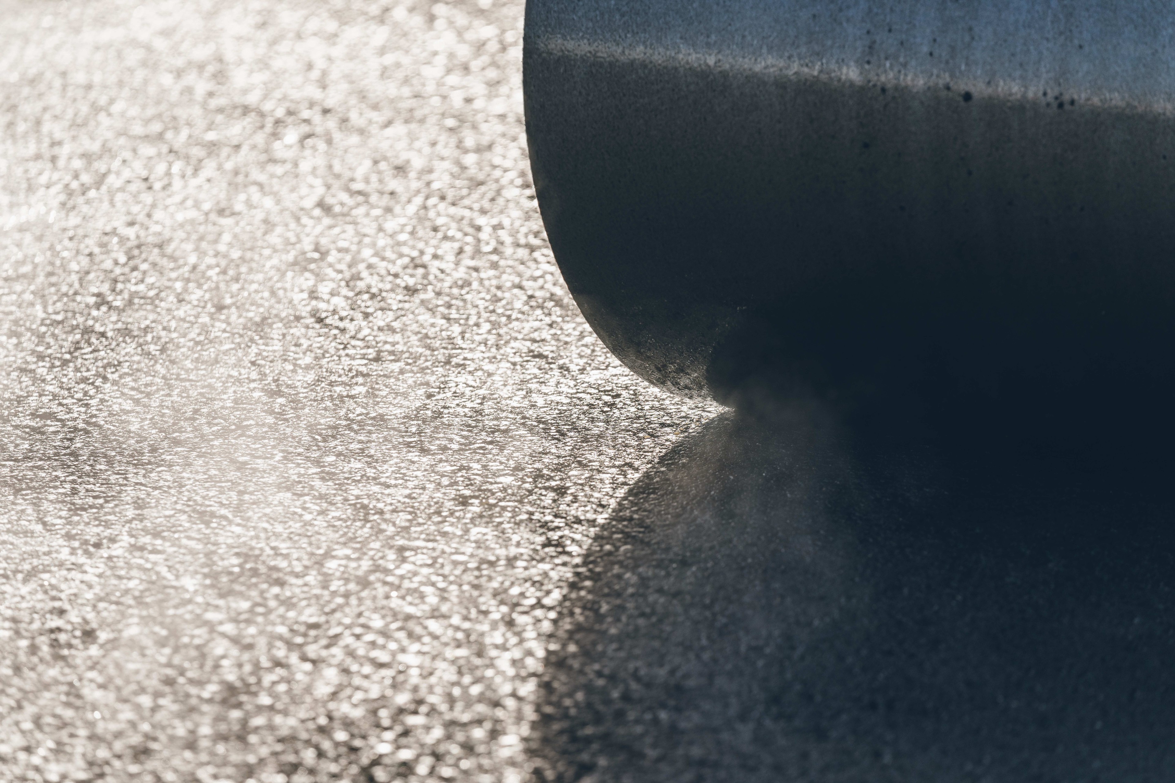 Roller that smooths fresh asphalt and creates a shiny, textured road surface in the sunshine.