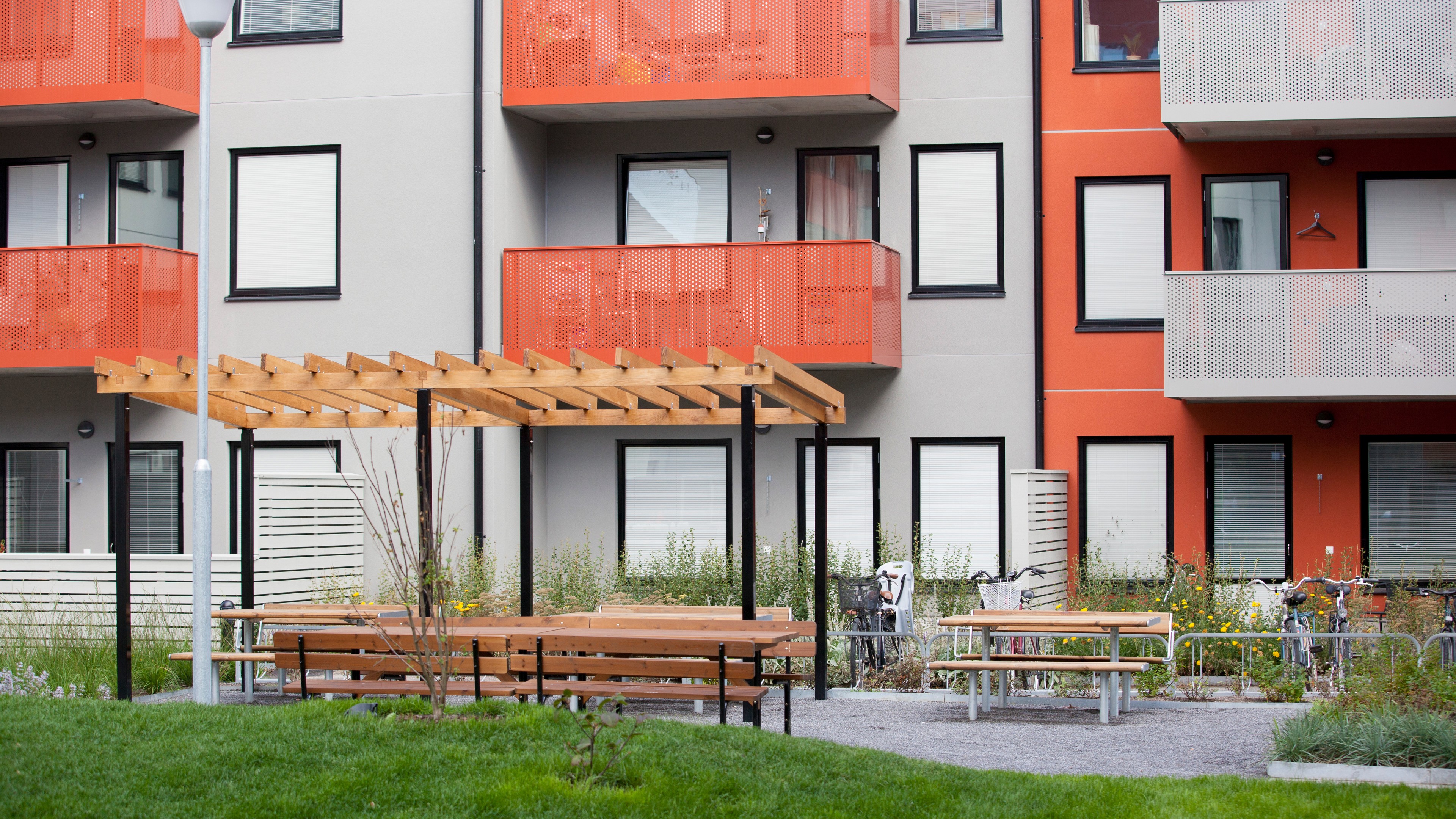Modern lägenhetsbyggnad med utomhus sittområde Modern lägenhetsbyggnad med orange balkonger och en träpergola i en anlagd innergård.