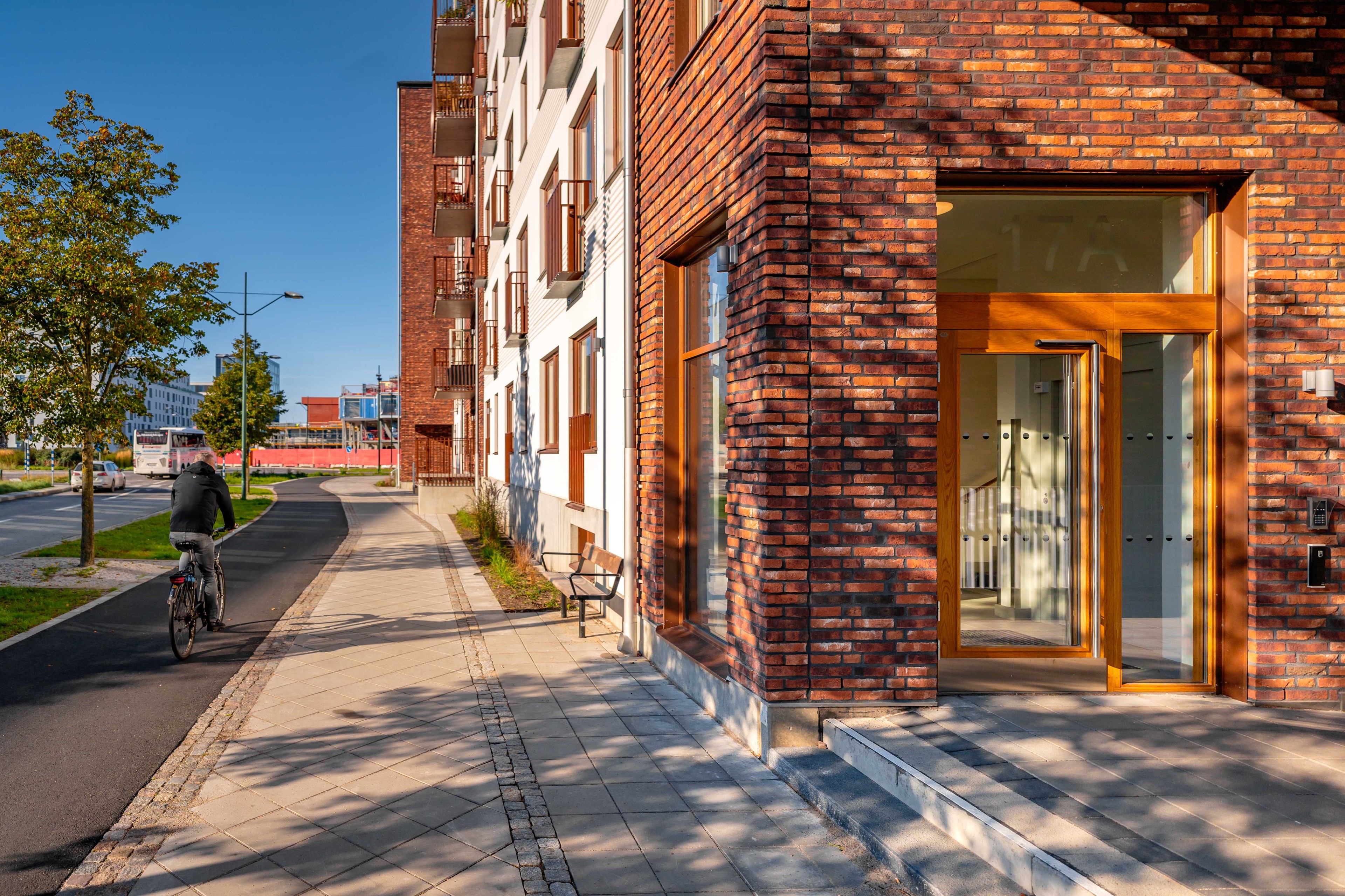 Modern urban lägenhetsbyggnad med cyklist på gångväg Modern stadsutsikt med cyklist, tegelbyggnad och klar himmel på en solig dag.